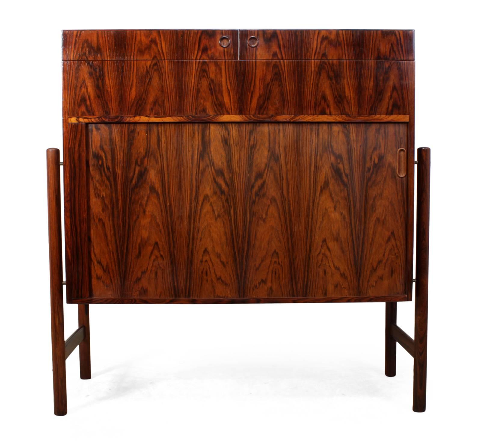 Midcentury dry bar in rosewood by Mogens Kold
A rare dry bar produced in Denmark by Mogens Kold in the mid-1960s, the bar has two flap over tops to reveal bottle holder and to create a long serving top, the lower section has a tambour sliding door