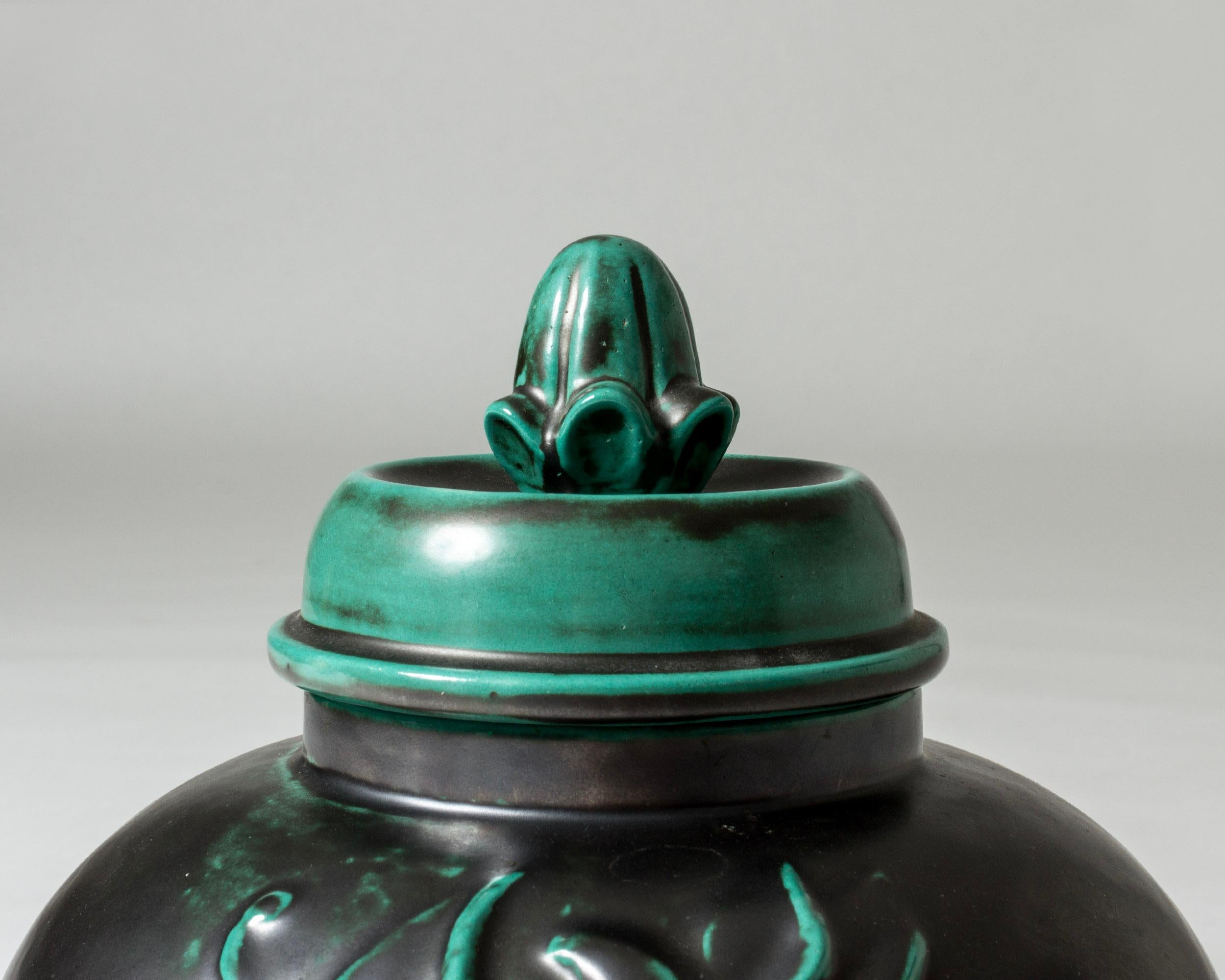 Striking, oversized earthenware jar by Anna-Lisa Thomson. Plump form with an embossed floral motif. Glased deep green with a lighter hue on the lid.