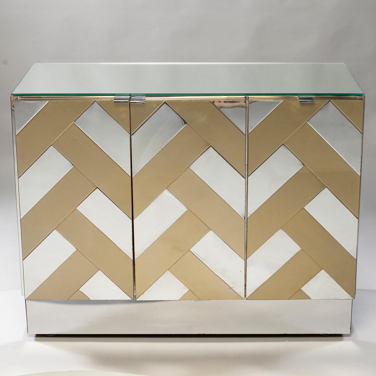 Ello Furniture cabinet has three hinged front doors that open to compartment with internal shelf, zig zag pattern in contrasting chrome and brass applied metal veneer mirrored top, circa 1970s.