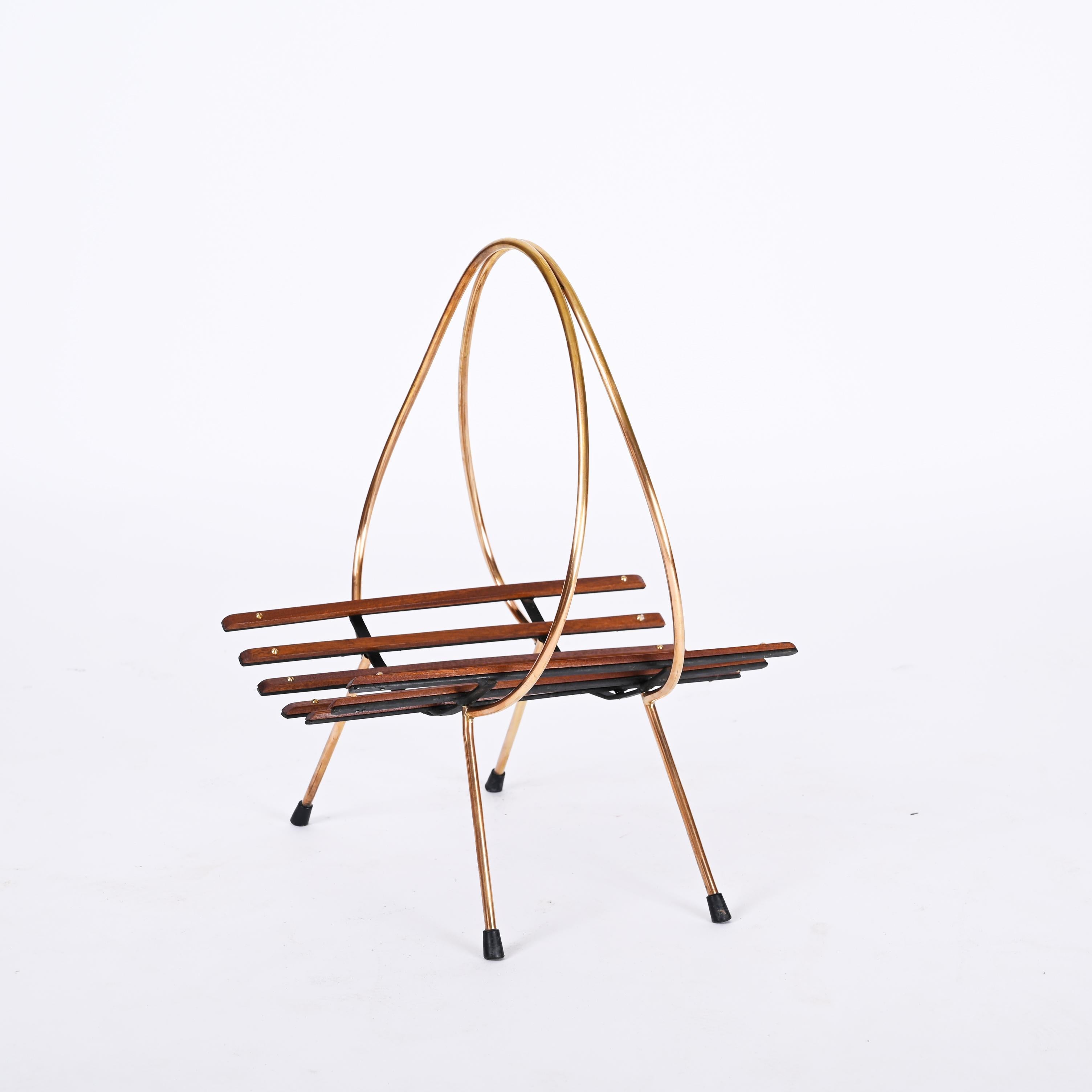 Beautiful and unique mid-century magazine rack in metal, teak and brass. This fantastic piece was produced in Italy during the 1960s.

The item is lovely as it has a gilded metal and brass structure and wood teak boards, working as a base for the