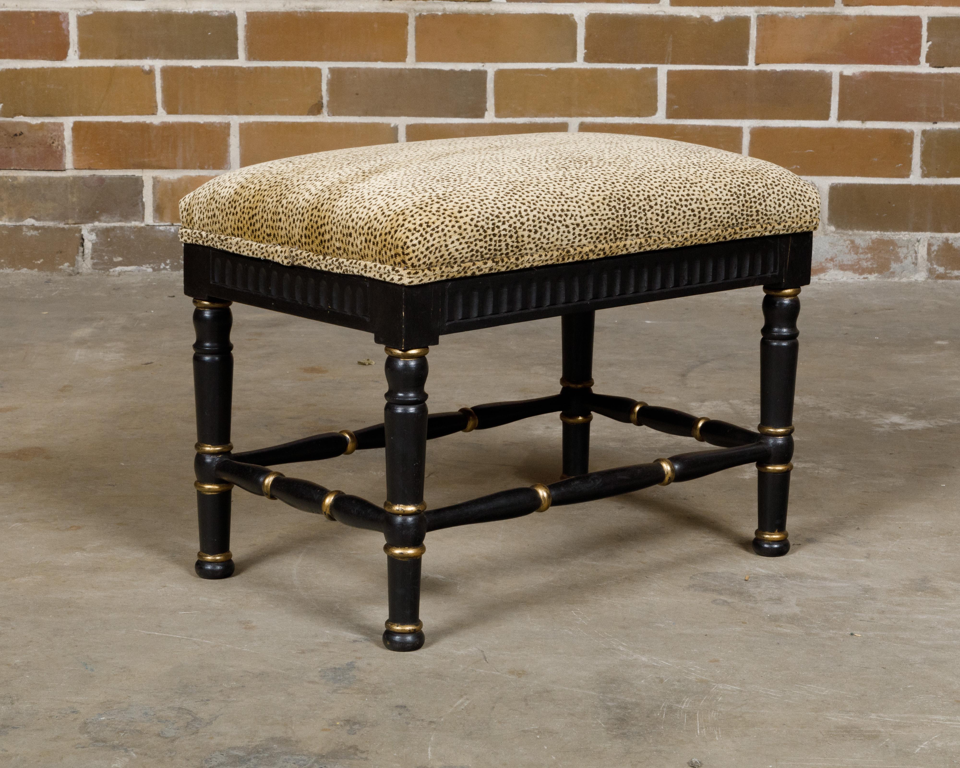 An English black and gold ebonized stool from the Midcentury period with leopard style upholstery. Born in mid-20th century England, this exquisite ebonized stool captivates with its striking black and gold finish and bold leopard-style upholstery.