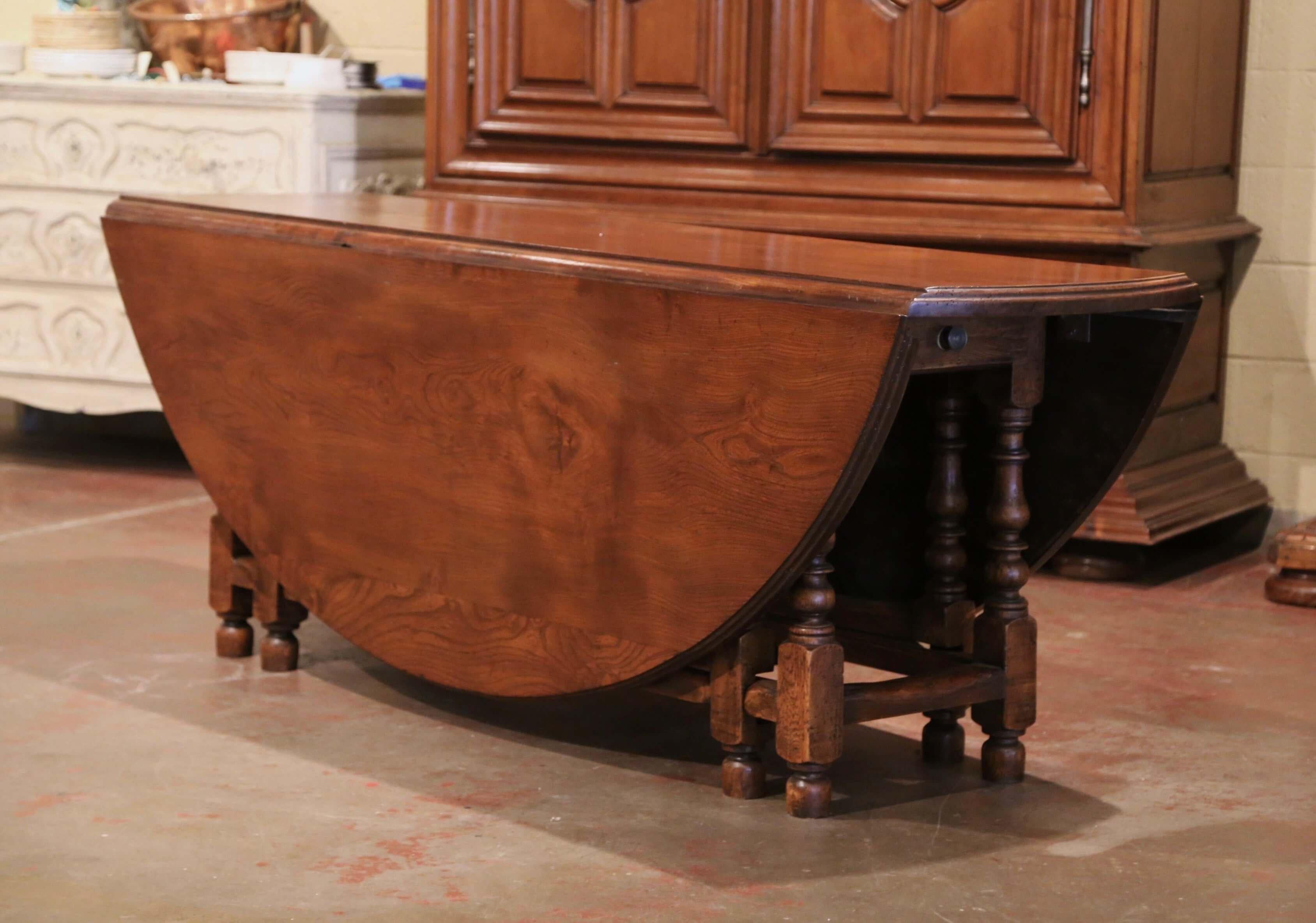 Crafted in England from solid chestnut, circa 1950, the large fruitwood dining room table stands on sturdy turned legs embellished with a decorative stretcher at the bottom. The table has four extra legs that unfold, and two large drop leaves come