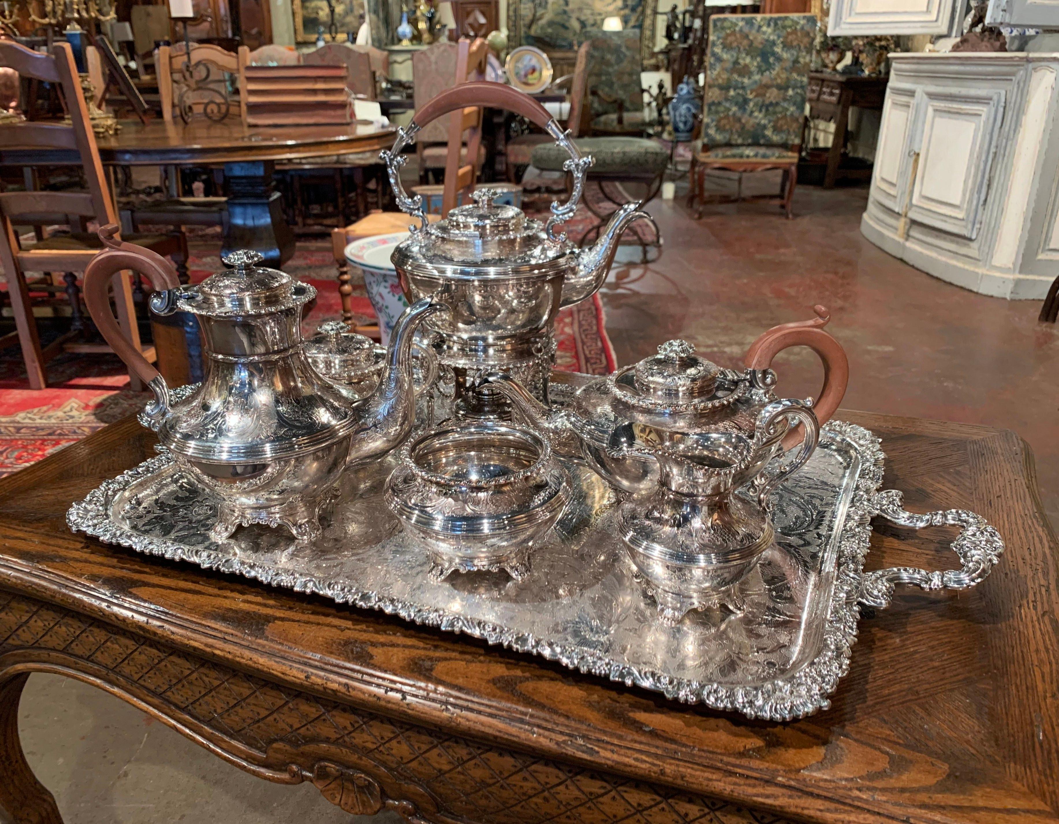 Crafted in England circa 1960, the seven-piece tea set is complete; the set stands on a beautiful paw footed tray and includes a coffeepot with a wooden handle, a teapot with wood handle, a kettle on stand with burner with oak handle, a covered