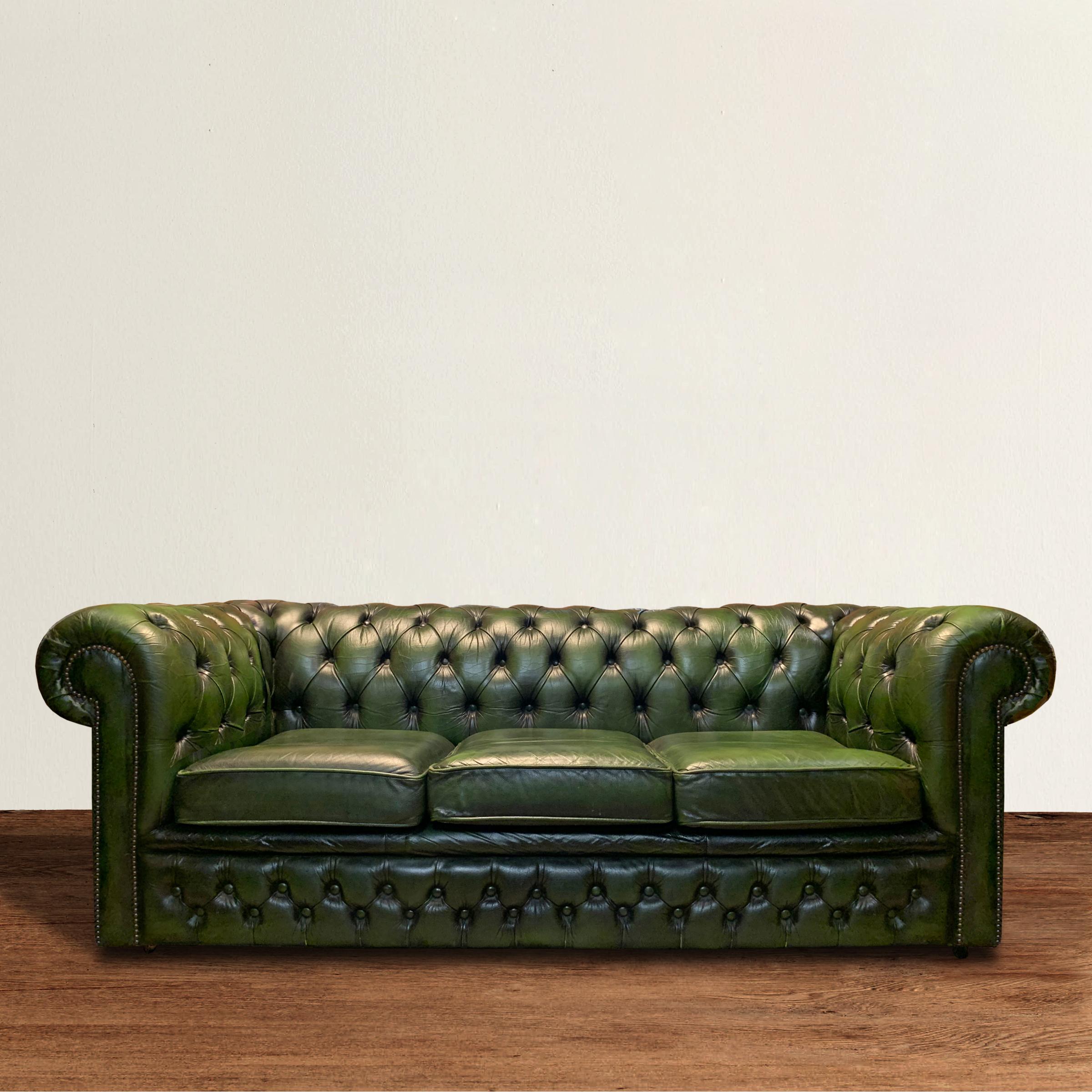 A quintessentially English mid-20th century emerald tufted Chesterfield sofa with a rich dark emerald green leather upholstery with three cushions, rolled and tufted arms and back, and a tufted front panel, all with brass nailhead trim. The sofa