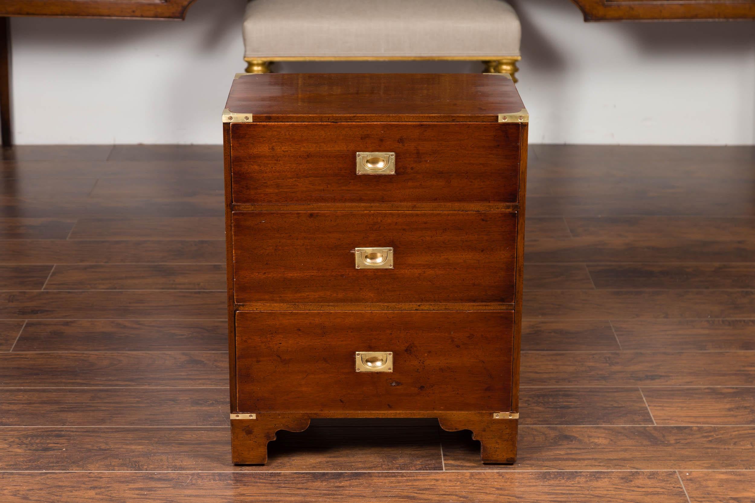 An English mahogany campaign chest from the mid-20th century, with three drawers, brass hardware and bracket feet. Born in England during the midcentury period, this campaign chest features a rectangular top sitting above three dovetailed drawers