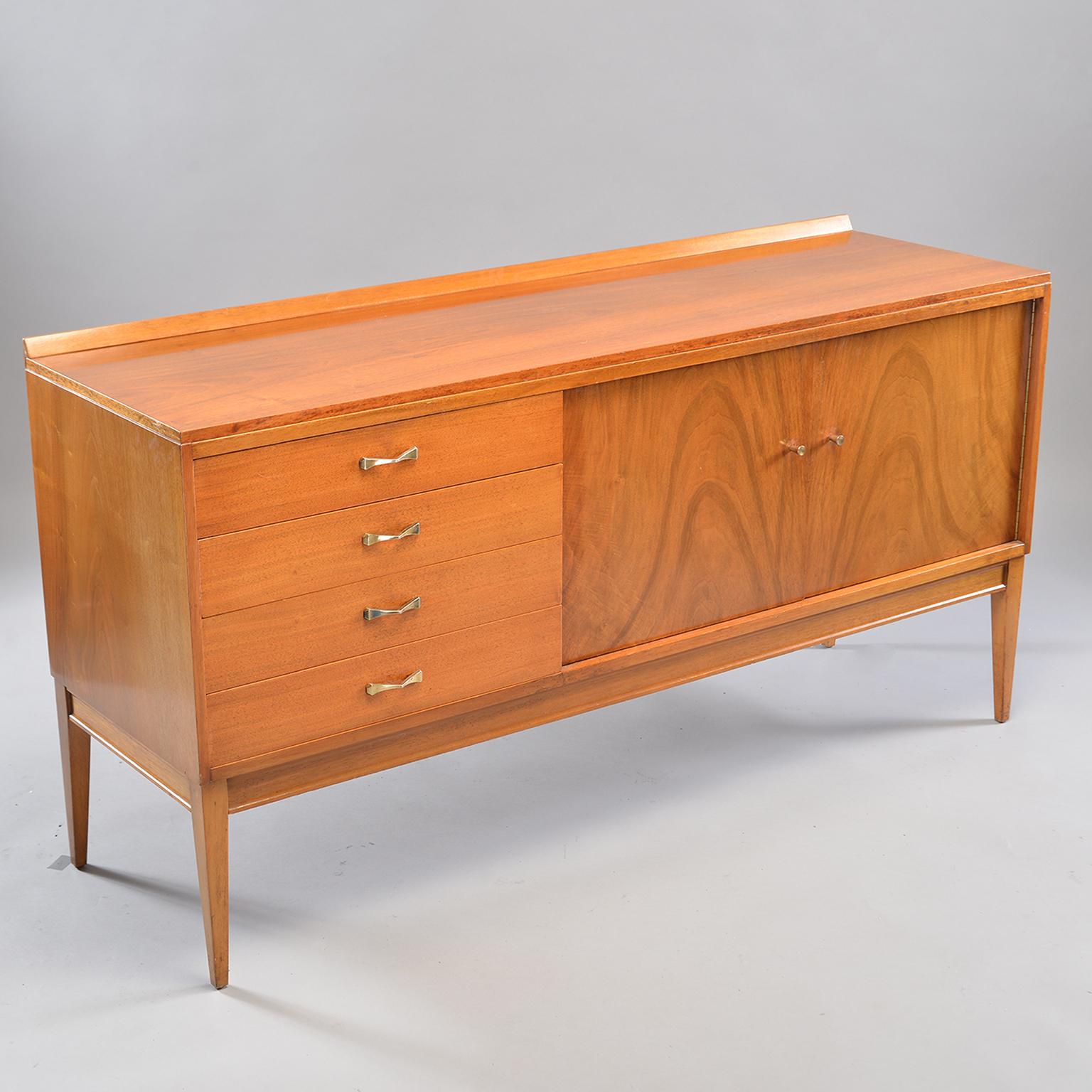 English blond walnut sideboard features four drawers and a cabinet section with an internal shelf, circa 1950s. Beautiful figuring on the two hinged doors. Tapered legs and brass hardware. Unknown maker.