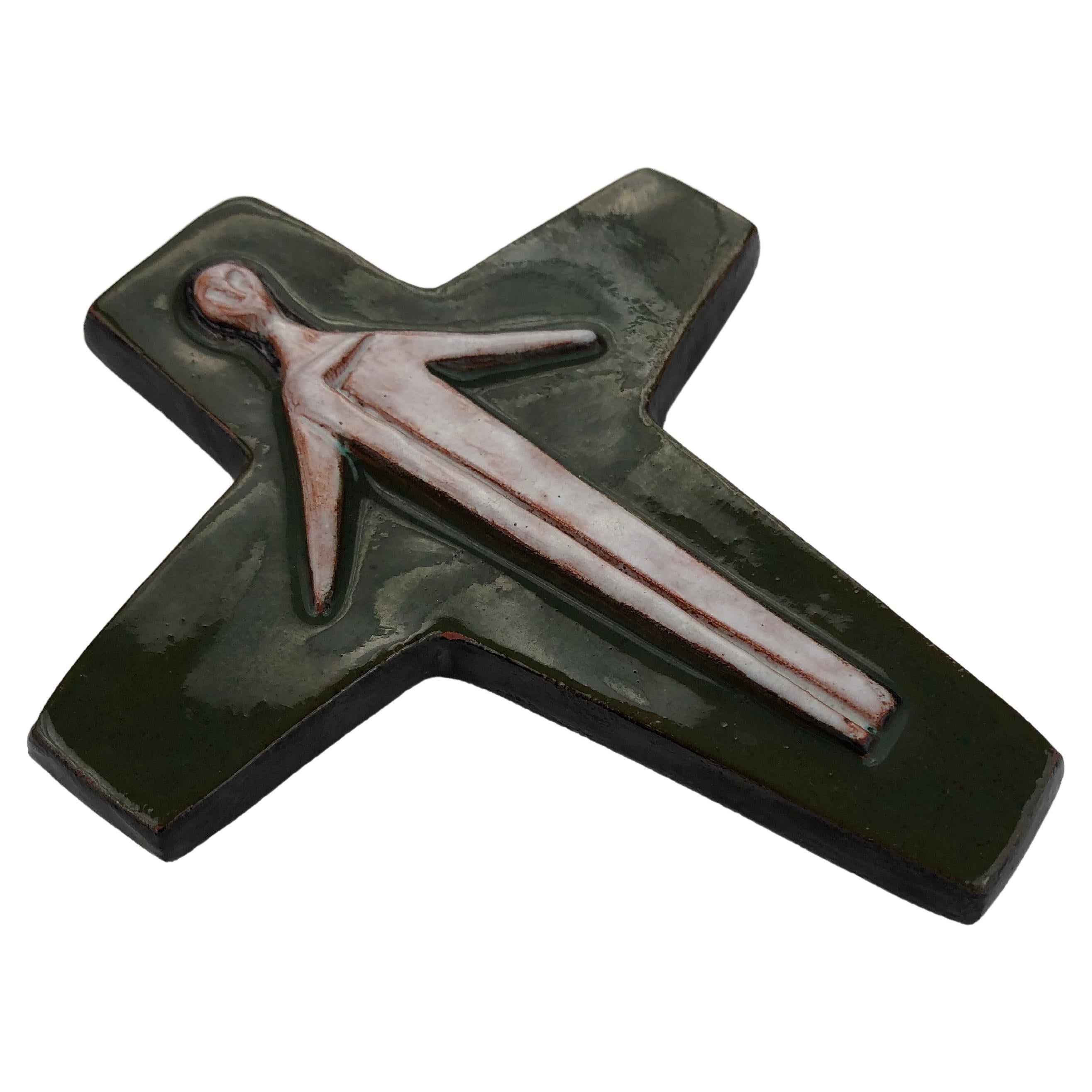 A brown green, glossy, midcentury ceramic cross with a minimal, otherworldly Christ figure. This piece is part of our large collection of crosses meticulously handmade by skilled Flemish artisans.

The enigmatic Christ figure is raised in matte