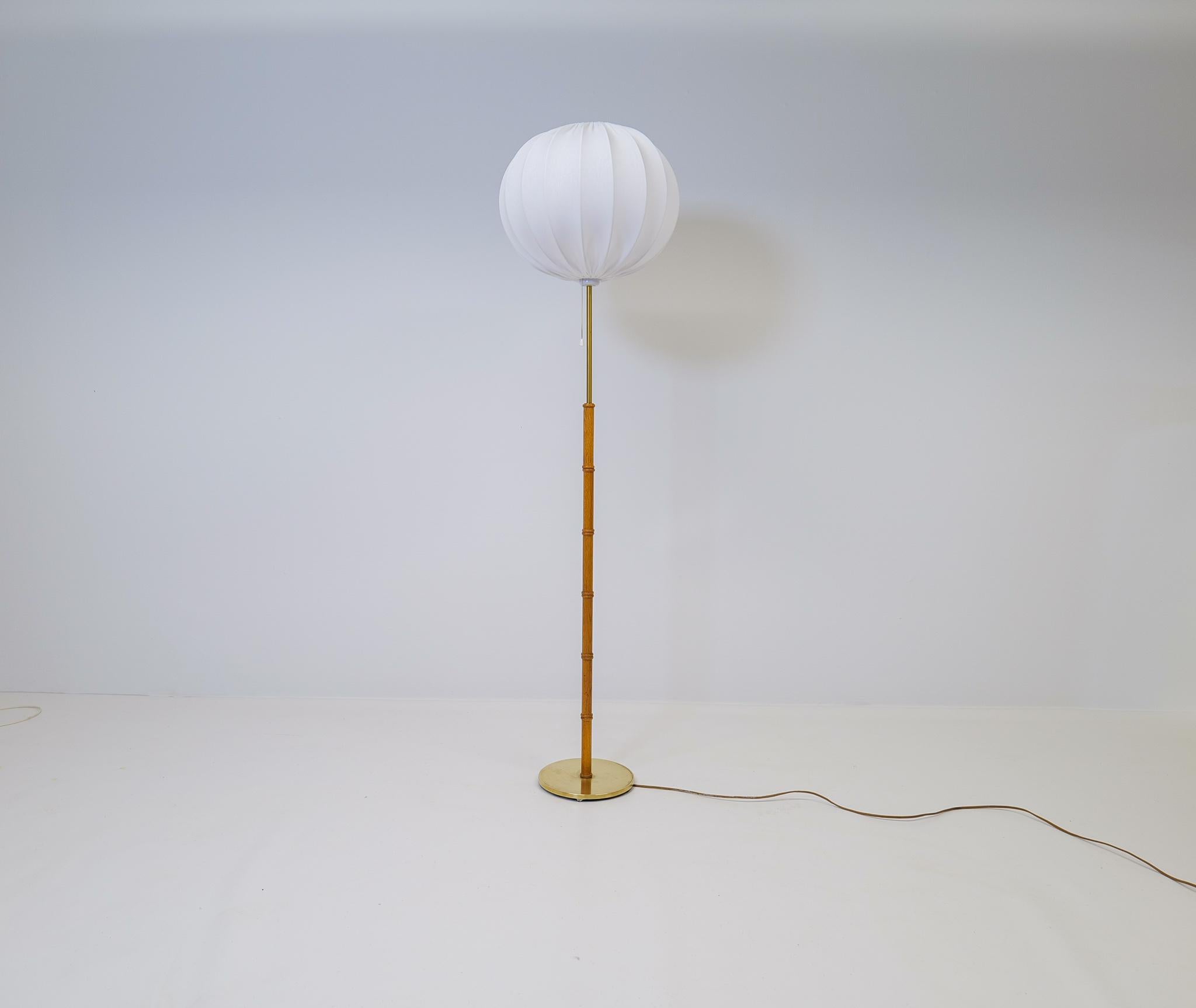 This lamp was made in Sweden at Falkenbergs Belysning. The combining of brass and oak makes this lamp a good piece of Swedish design. New quality round shade made in Sweden.

Good working condition with some dents on the foot and scratches on the