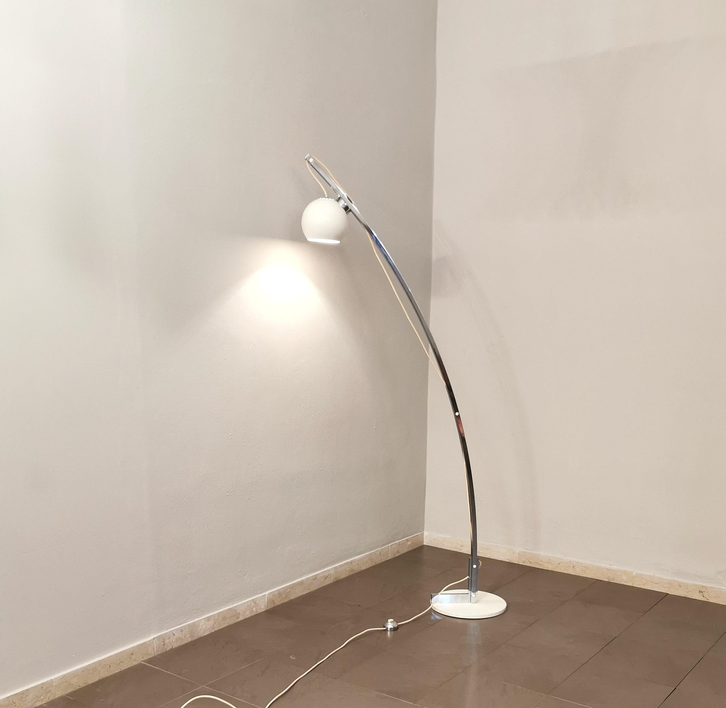 Design floor lamp in the style of Goffredo Reggiani, produced in Italy in the 70s. The lamp has a circular base in white enamelled metal, where a curved stem in chromed metal stands, which thanks to its wire and its magnet supports a half-sphere
