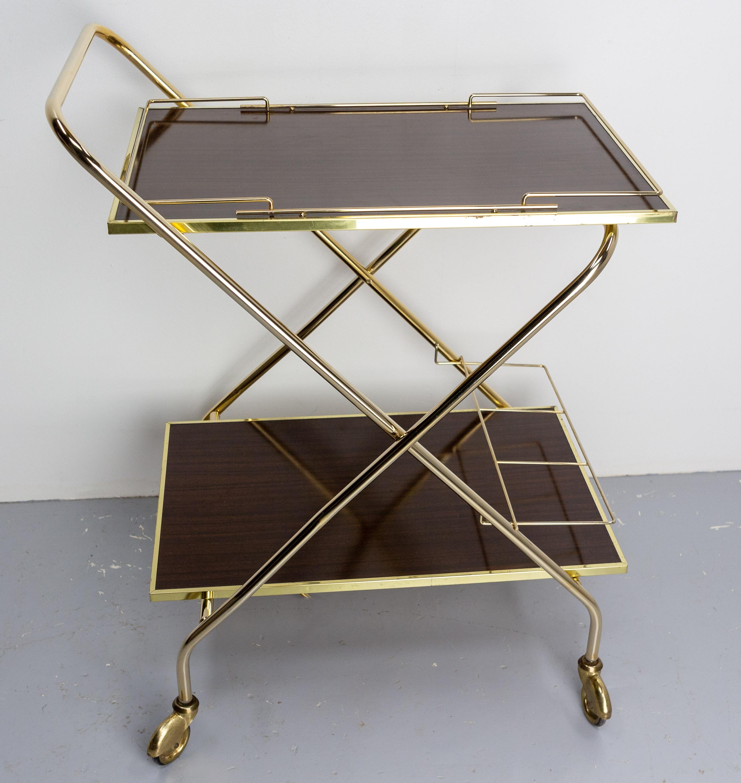 Dark wood laminate and golden chrome serving trolley folding bar cart drinks midcentury, august 1976
In good working order.
Easy to fold.
Very good vintage condition.

Measures when folded: D 19.68 in. / W 40.94 in. / H 7.48 in. (D 50 / W 104 /