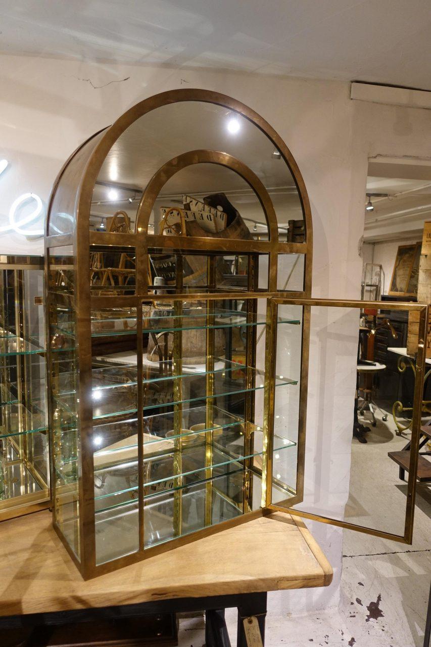 Absolutely stunning midcentury display cabinet with a supremely elegant arched top. Made of quality brass, beautifully patinated over many years. Behind the cabinet door are 3 glass shelves with adjustable brass height brackets.

Originating from