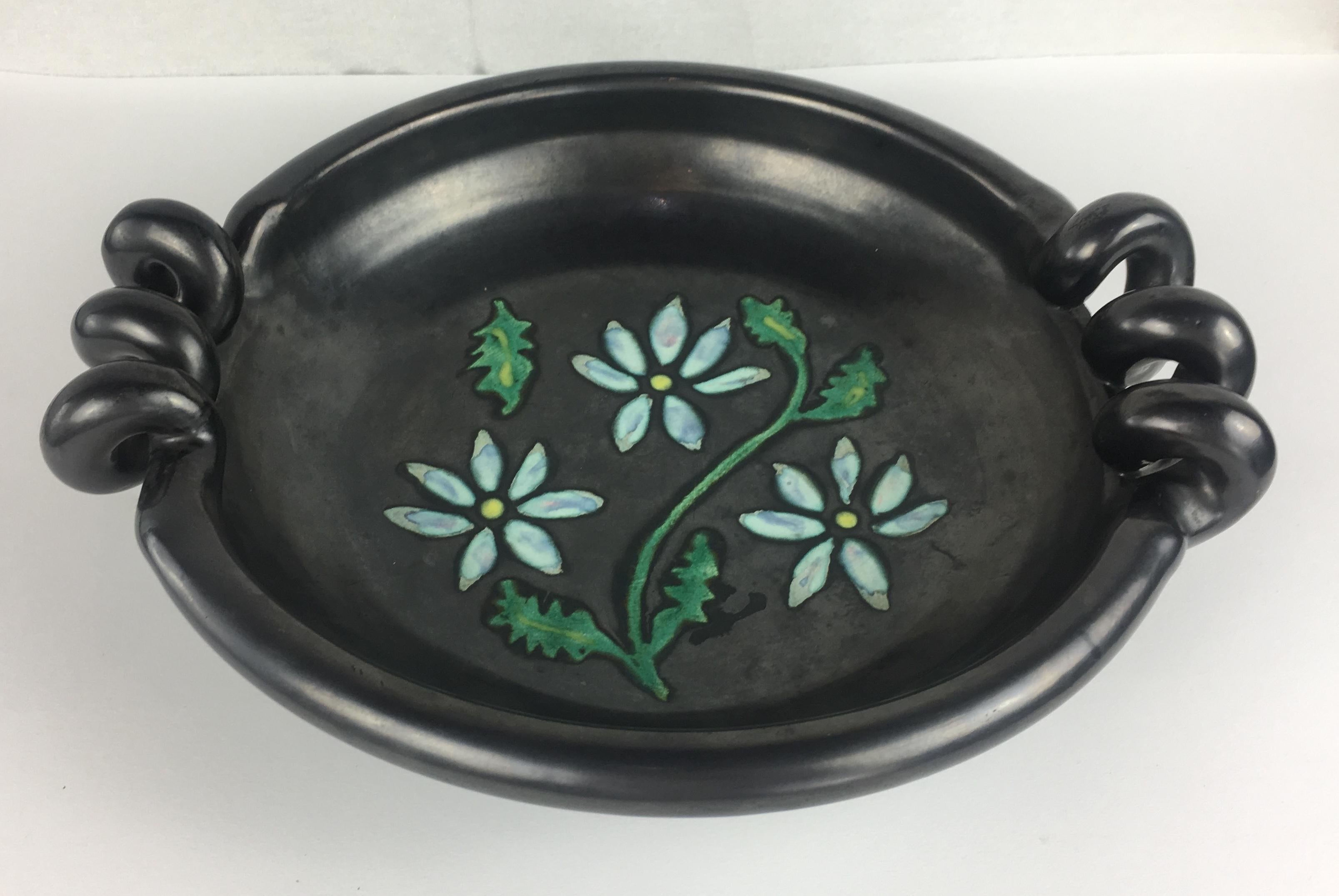 Midcentury sculptural bowl with a very nice black matte finish with floral design in the center and rope style handles. Signed and most likely from Vallauris.

This interesting semi-glazed piece will look good on any coffee table or countertop. It