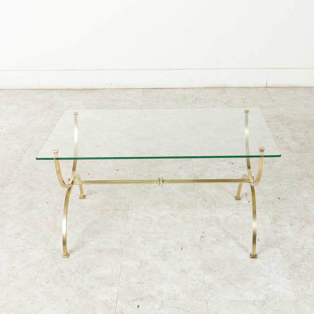 Found in the Languedoc region of southern France, this midcentury brass coffee table features a thick glass top with gently rounded corners. The legs of the base are formed by two opposing half circles and are connected by a central stretcher that