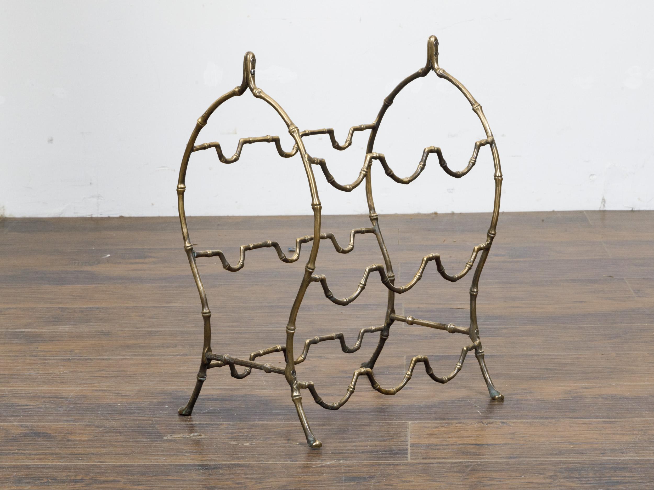 A French brass faux bamboo wine rack from the mid 20th century with arching side supports and pad feet. This charming French brass faux bamboo wine rack from the mid-20th century brings an elegant touch of vintage flair to any home decor. The rack