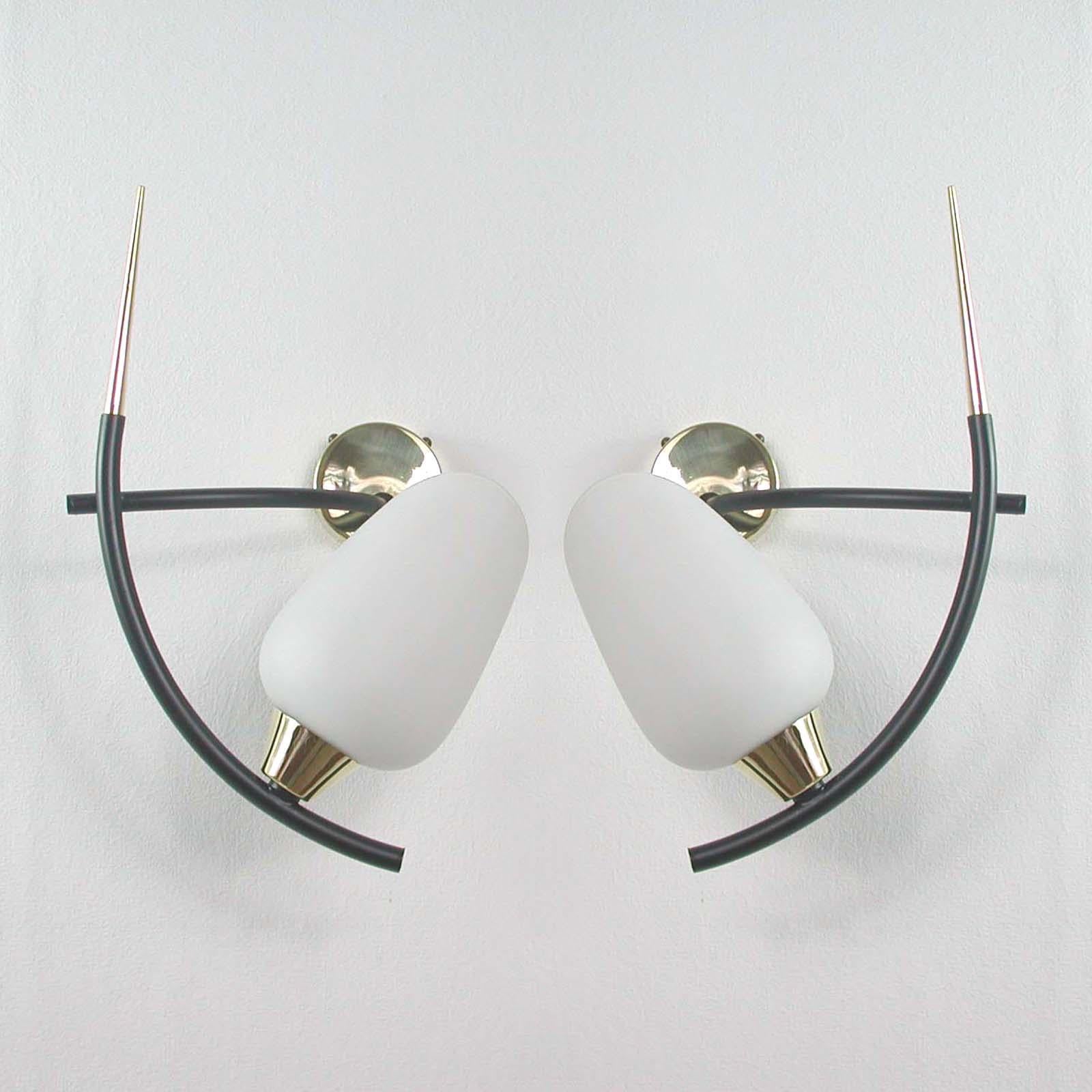 This awesome pair of French sconces was designed and manufactured by Maison Arlus in the 1950s. The lights are made of black lacquered metal and polished brass with an asymmetrical opaline glass lamp shades. The lamp arms can be turned in different