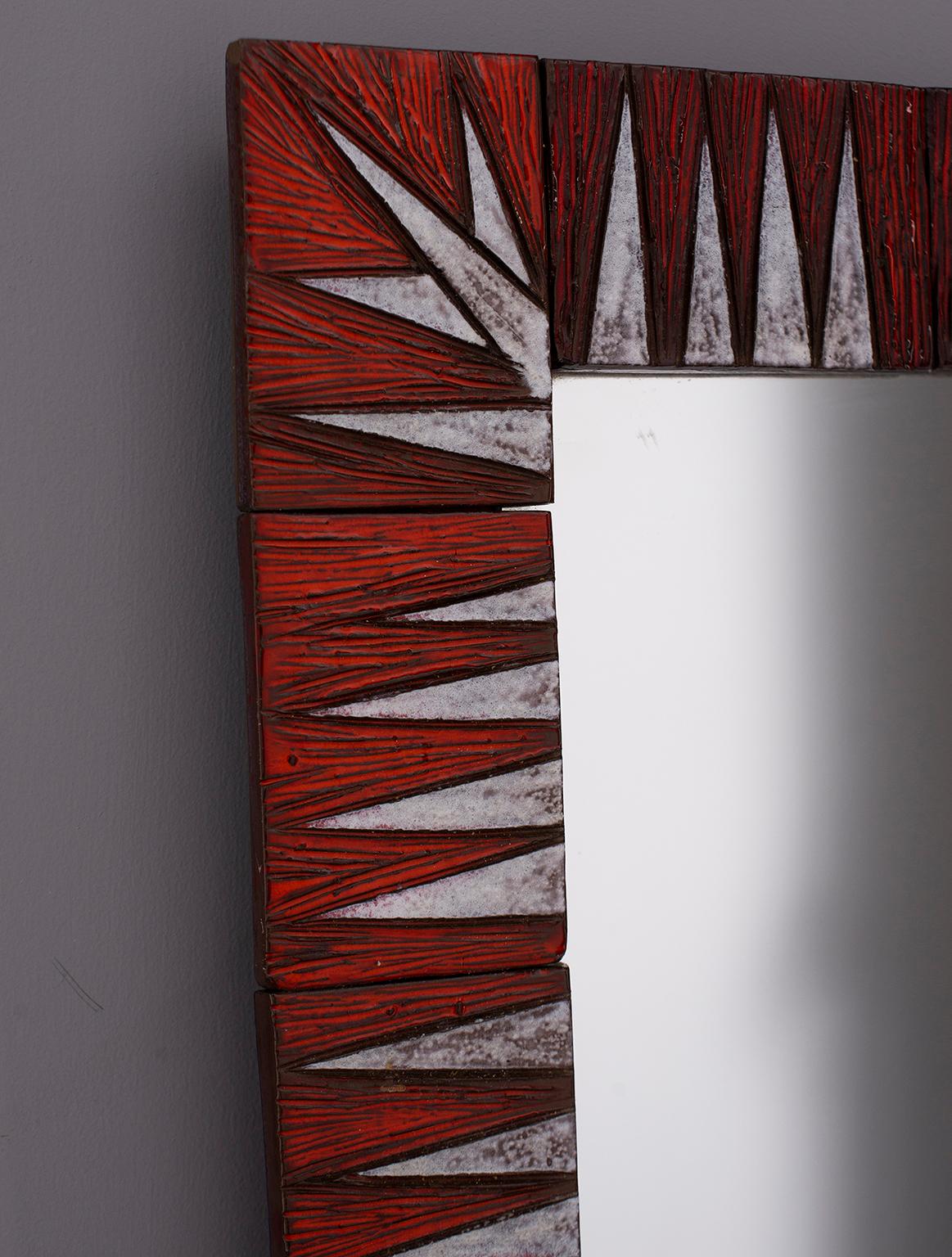 French rectangular mirror has ceramic frame with red and white etched and glazed finish, circa 1970s. Handmade ceramic tiles form a striking pattern of blade that border the mirror. Unknown maker.