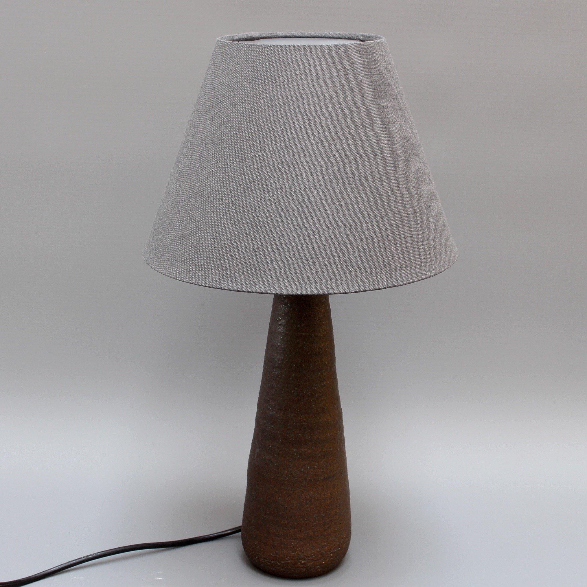 Midcentury French ceramic table lamp by Jean Rivier (circa 1960s). A conically shaped lamp of earthenware with a subtle molten green glaze over the brown matt surface. The clay was layered in coils to form the conical shape and the surface is