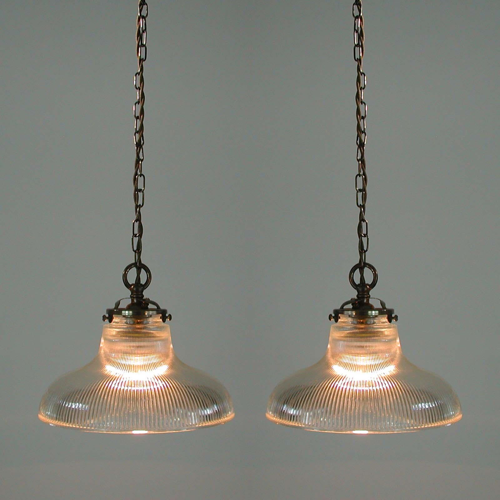 These Art Deco style dome shaped pendant lights were made in France in the 1950s. They feature a clear prismatic glass Holophane lamp shade and patinated brass glass holder, chain and canopy. 

The glass gives off the best quality light. It is