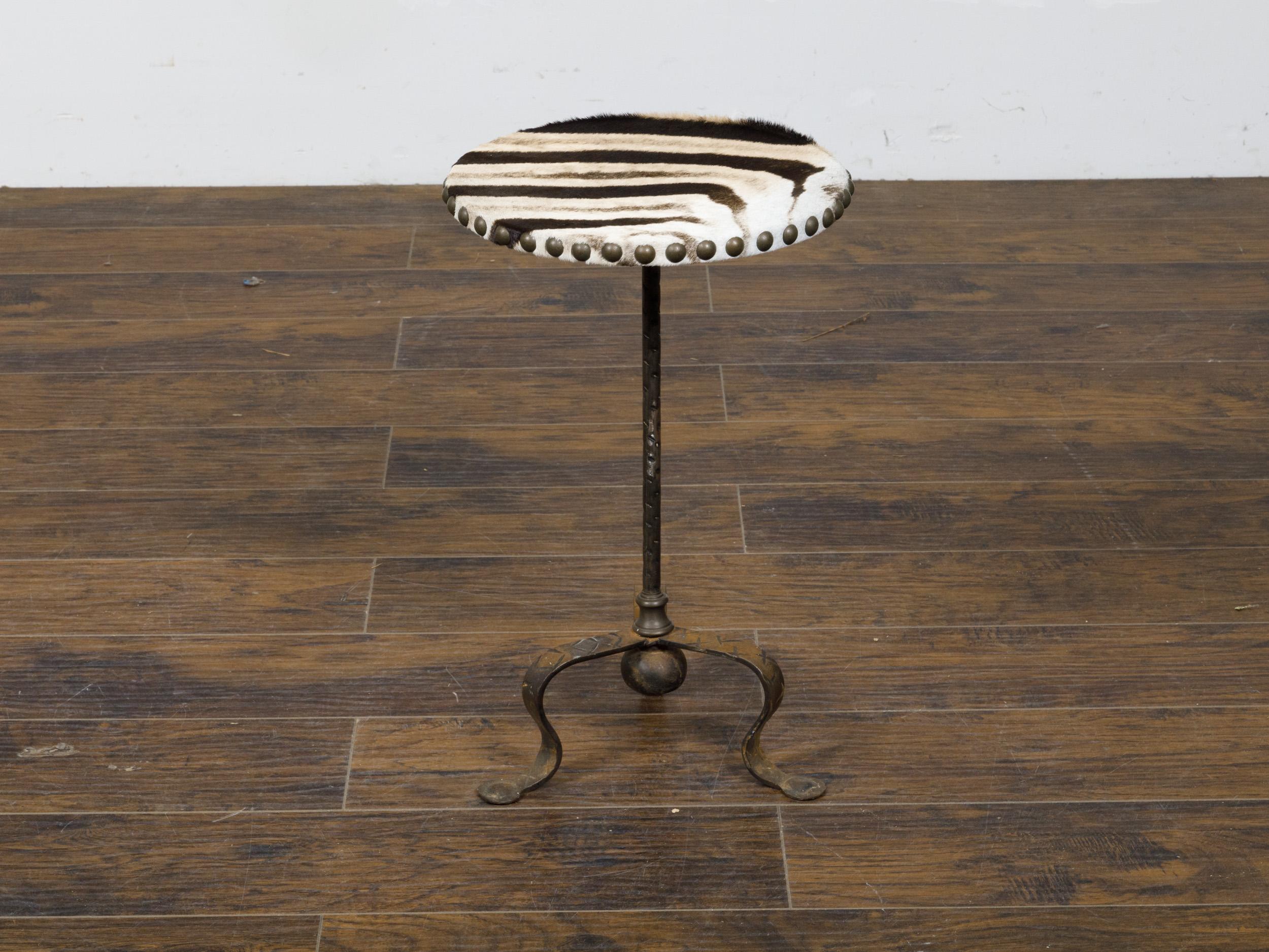 A French iron guéridon side table from the mid 20th century with circular zebra hide top and tripod base. This striking mid-20th century French guéridon side table beautifully combines rugged and refined elements, creating a piece that is both