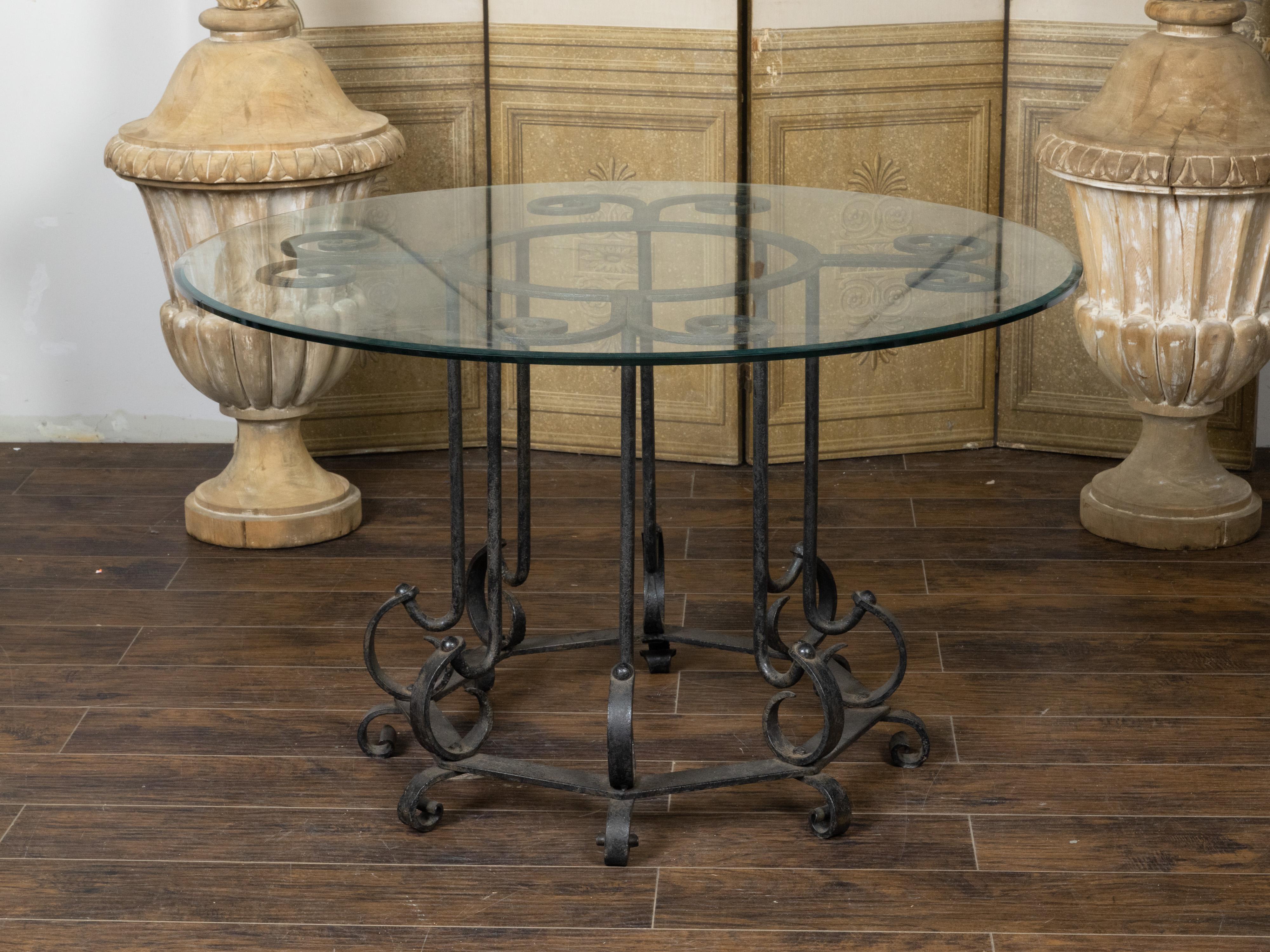 A vintage French iron center table from the mid 20th century with circular glass top, scrolling motifs and octagonal base. Created in France during the Midcentury period, this center table features a round glass top sitting above an elaborate iron