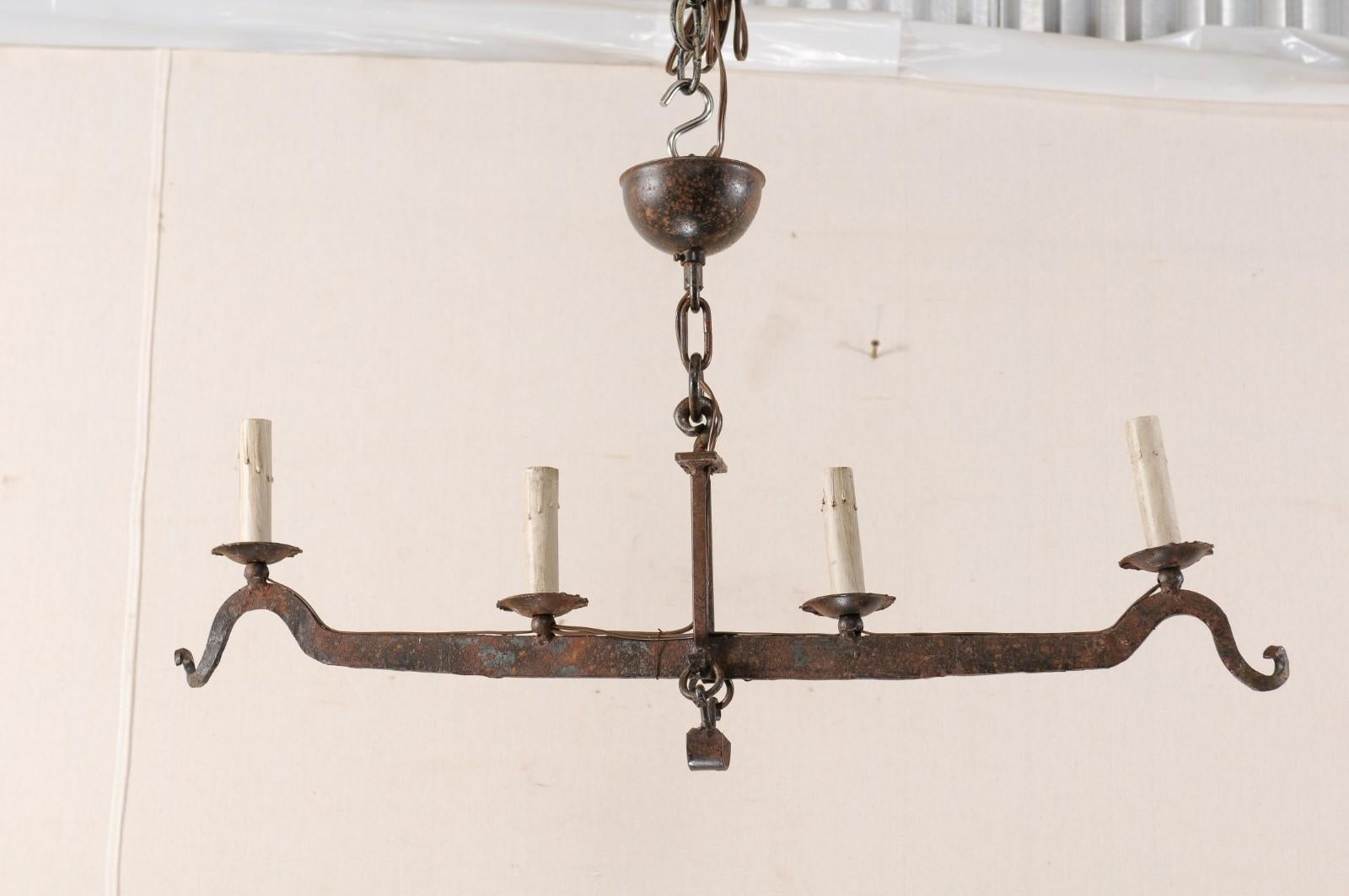 A midcentury French iron scale four-light chandelier. This vintage chandelier from France features an elongated central bar, which is part of an old scale, with hooked ends, and connected to top at center with a caged ridged double bar post. Four