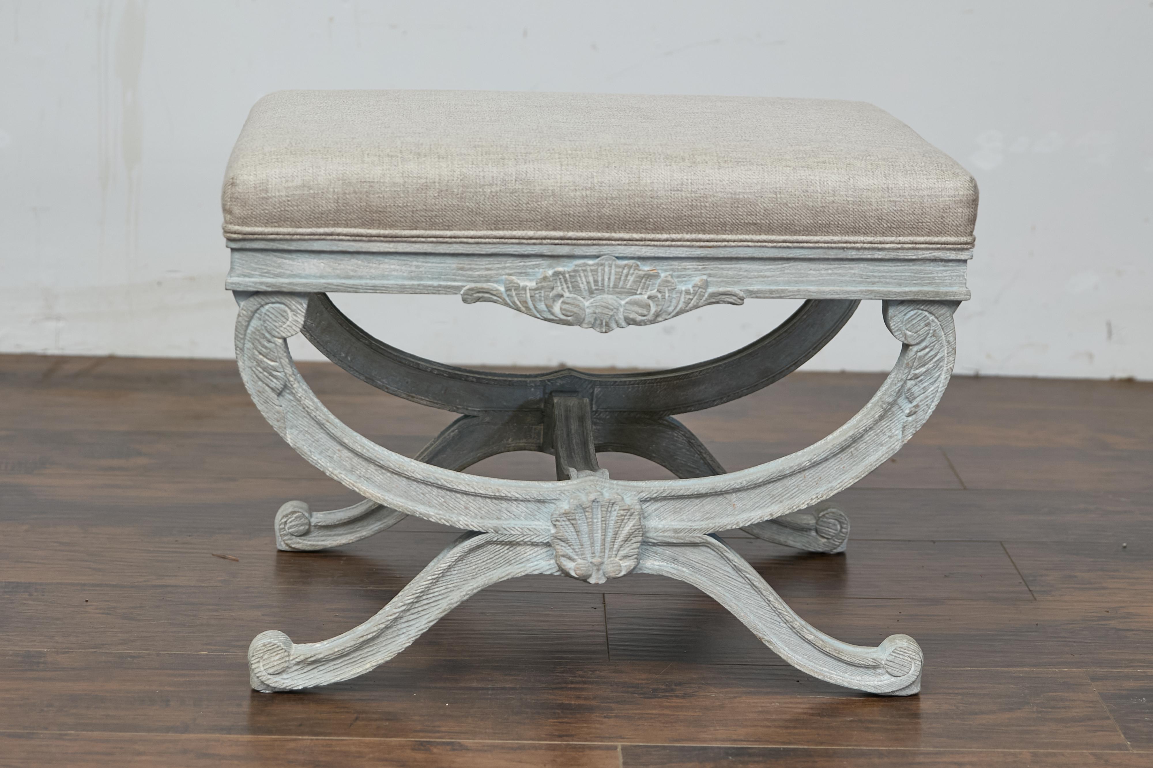 Sgabello francese di metà secolo dipinto di blu grigio chiaro a forma di Curule con motivi di conchiglie e fogliame intagliati, piedi a spirale e rivestimento in lino personalizzato. Questo elegante sgabello francese del Midcentury cattura