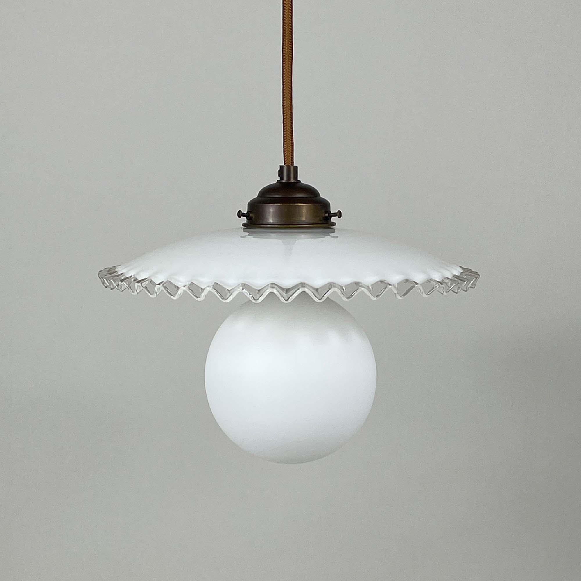 Cette lampe suspendue a été conçue et fabriquée en France dans les années 1950. La lampe est dotée d'un abat-jour en verre plissé blanc opalin et d'un support en laiton bronzé. Elle nécessite une ampoule E27 jusqu'à 60 Watt (LED recommandée) et a