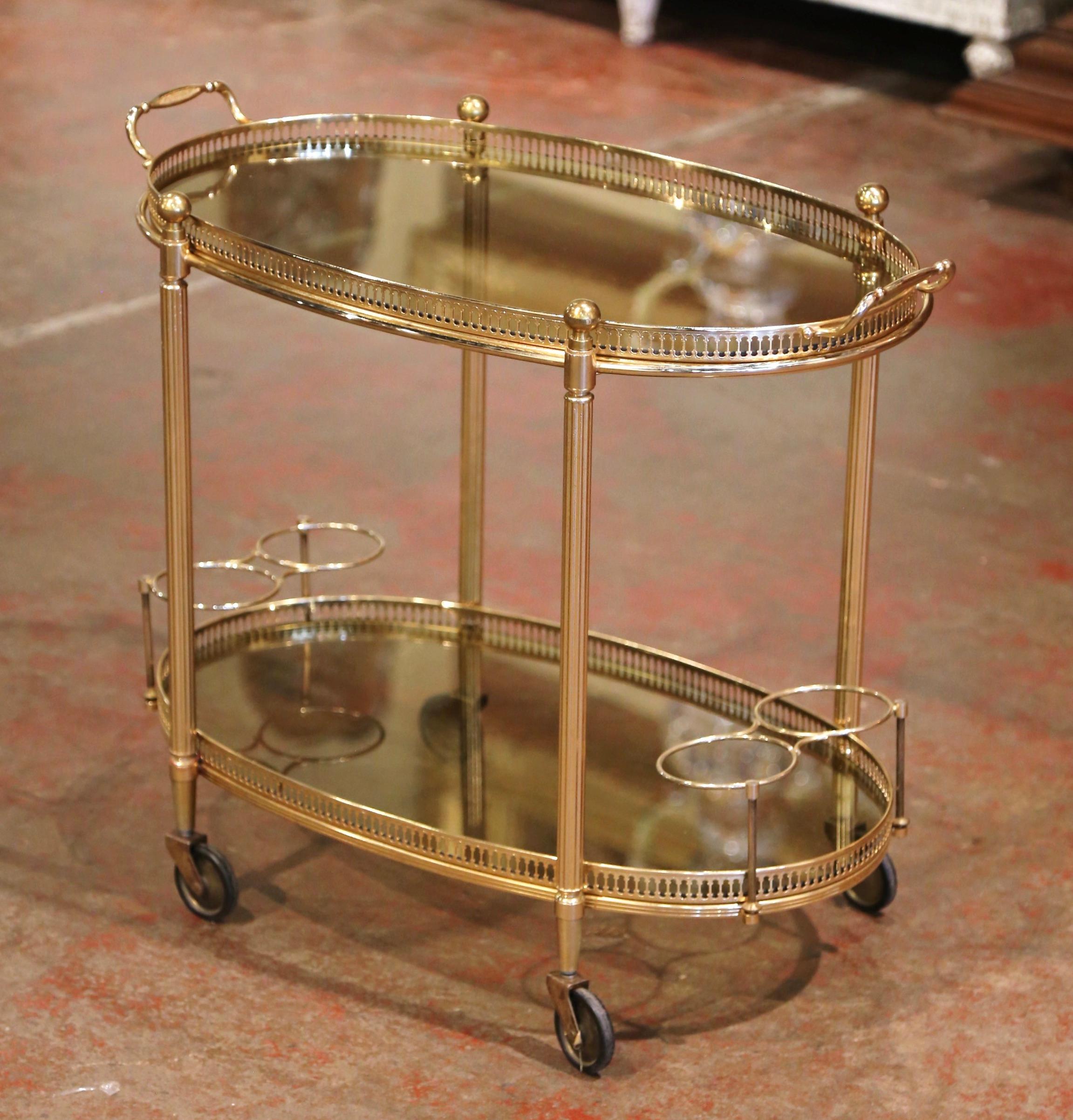 This beautiful, vintage two-tier rolling bar cart was created in France, circa 1950. Built in brass and oval in shape, the dessert table stands on small round wheels with rubber tires, over two plateaus topped with glass surfaces. The top deck