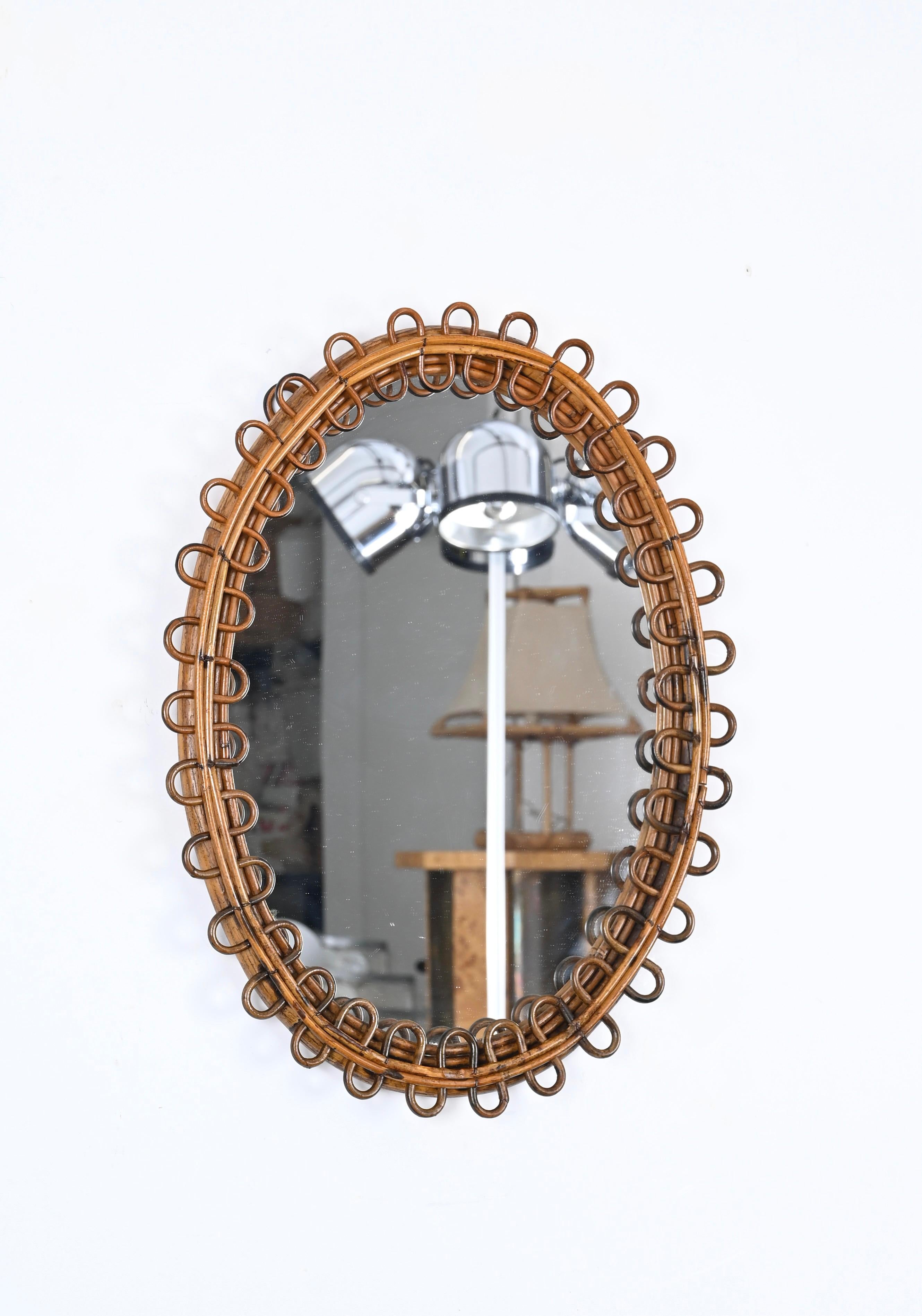Lovely decorative midcentury oval mirror with curved rattan beams and bamboo frame. This beautiful French Riviera style mirror was produced in Italy in the 1960s.

The mirror features a gorgeous oval double frame in curved bamboo enriched all around