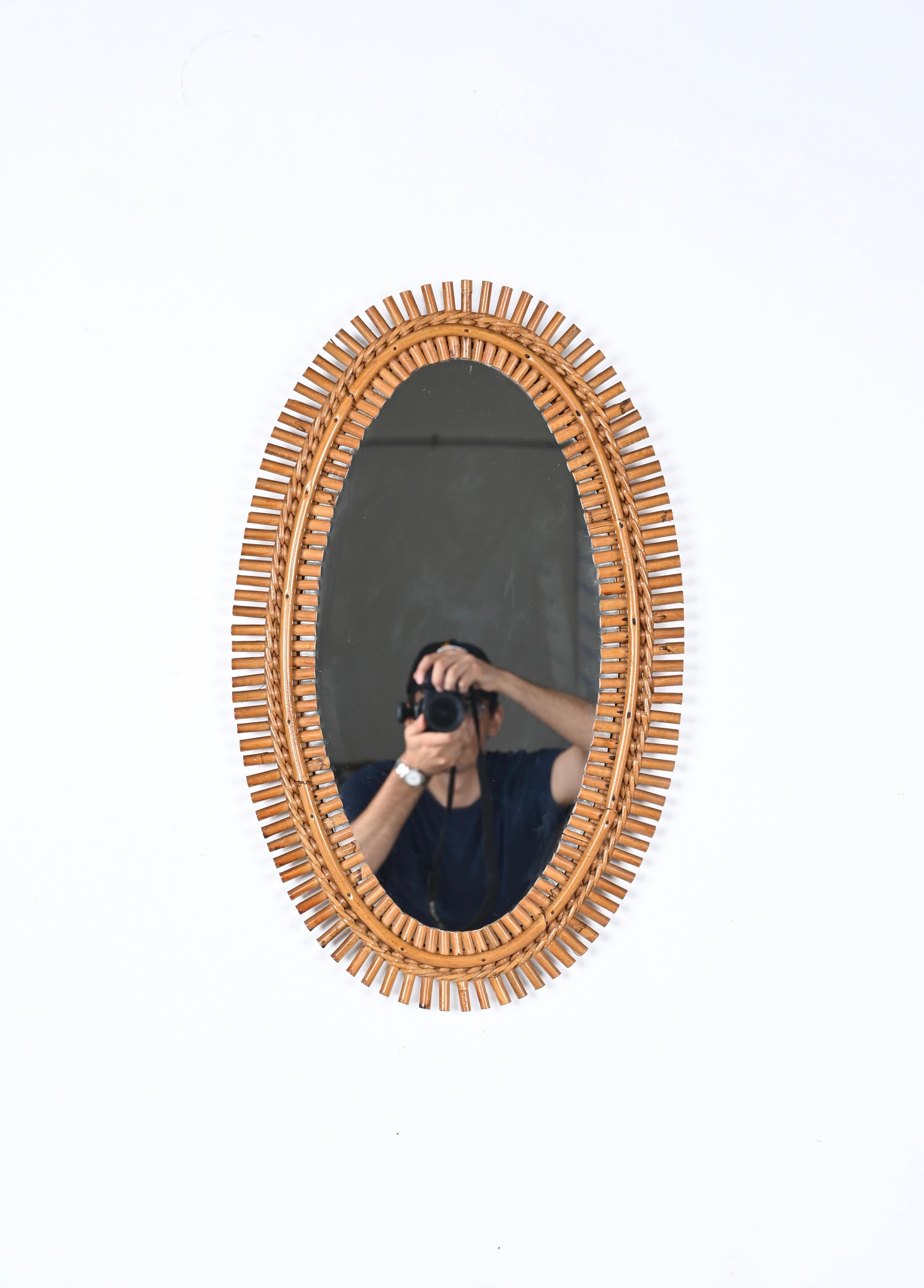 Gorgeous Cote d'Azur style oval mirror in bamboo, rattan and wicker, made in France in the 1960s. 

This lovely mirror features a double frame in curved rattan crossed by small bamboo inserts, the whole is kept together by a wonderful braid in