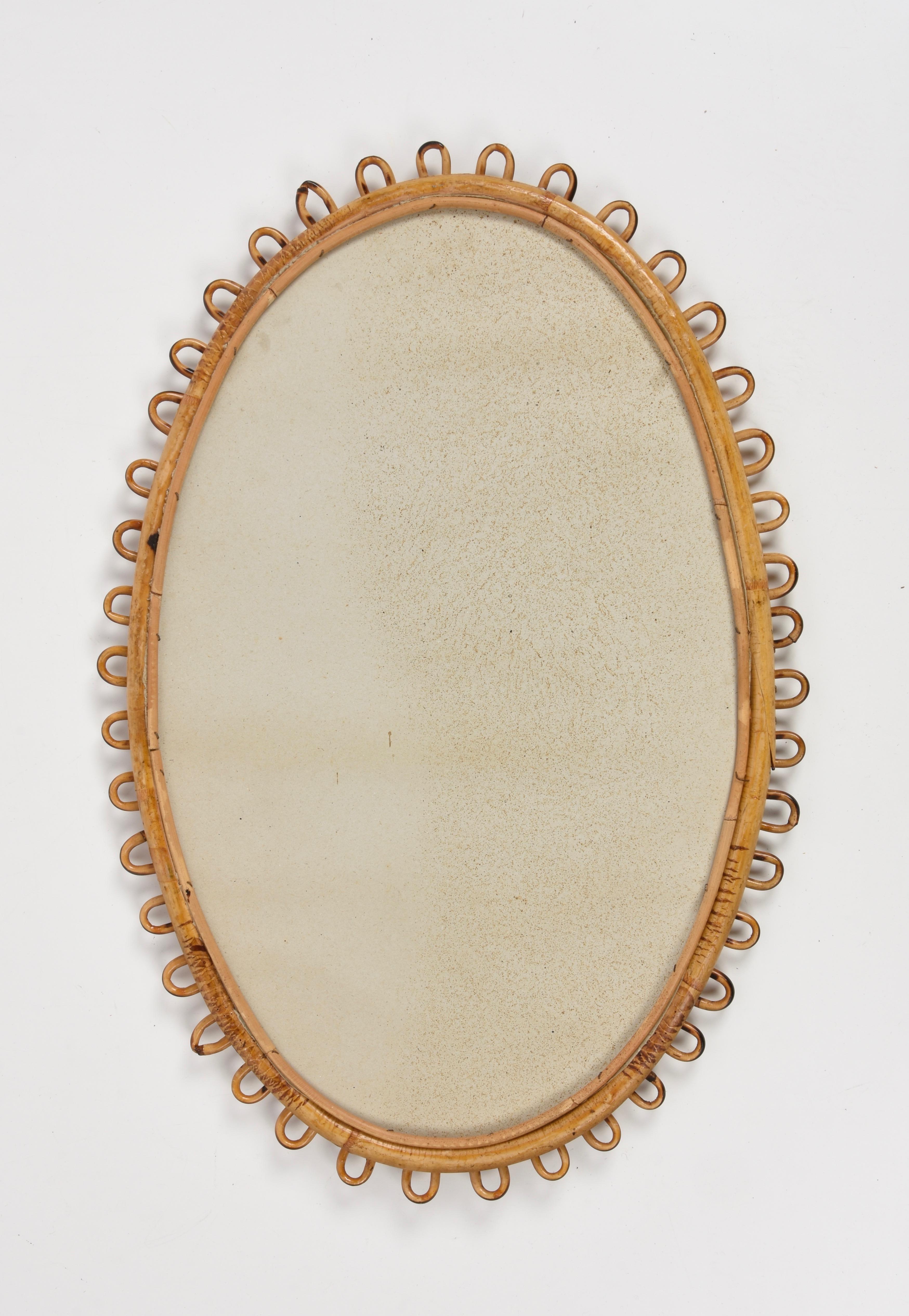 Midcentury decorative oval mirror with curved rattan beams and bamboo frame. This marvellous item was made in Italy during the 1950s.

This piece is unique as it has a sinusoidal rattan frame adding fine and elegant lines to its design.

The