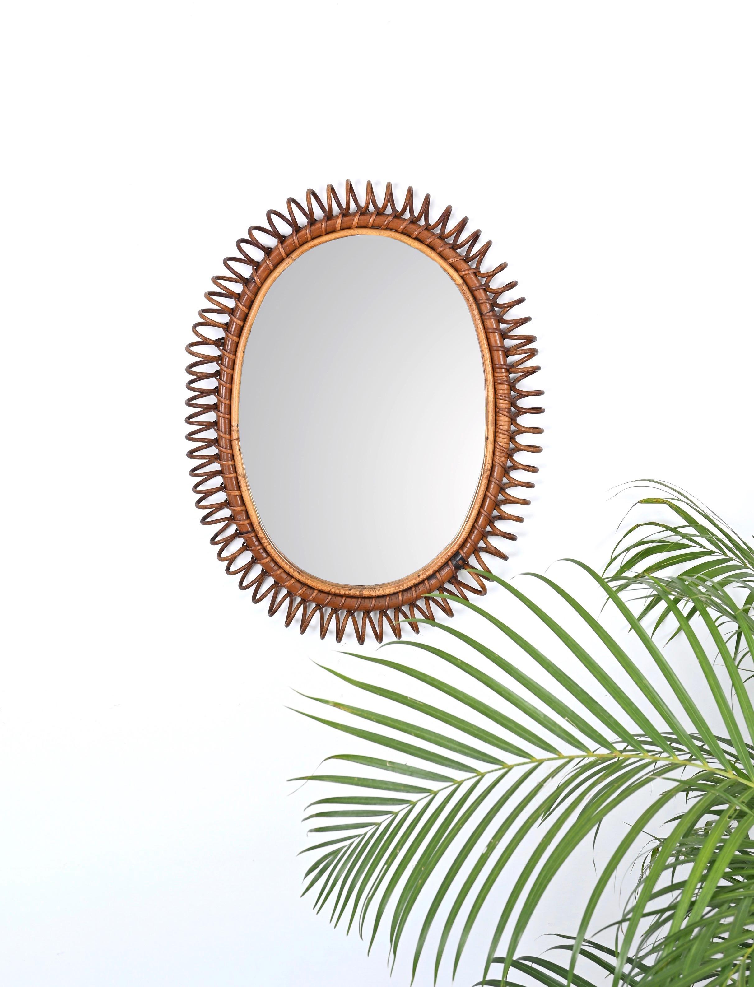 Marvelous midcentury oval mirror in curved rattan, bamboo and wicker. This fantastic piece was designed in Italy during the 1960s in Cote D'Azur style. 

This large mirror features a lovely spiral-shaped frame in curved rattan and wicker with an