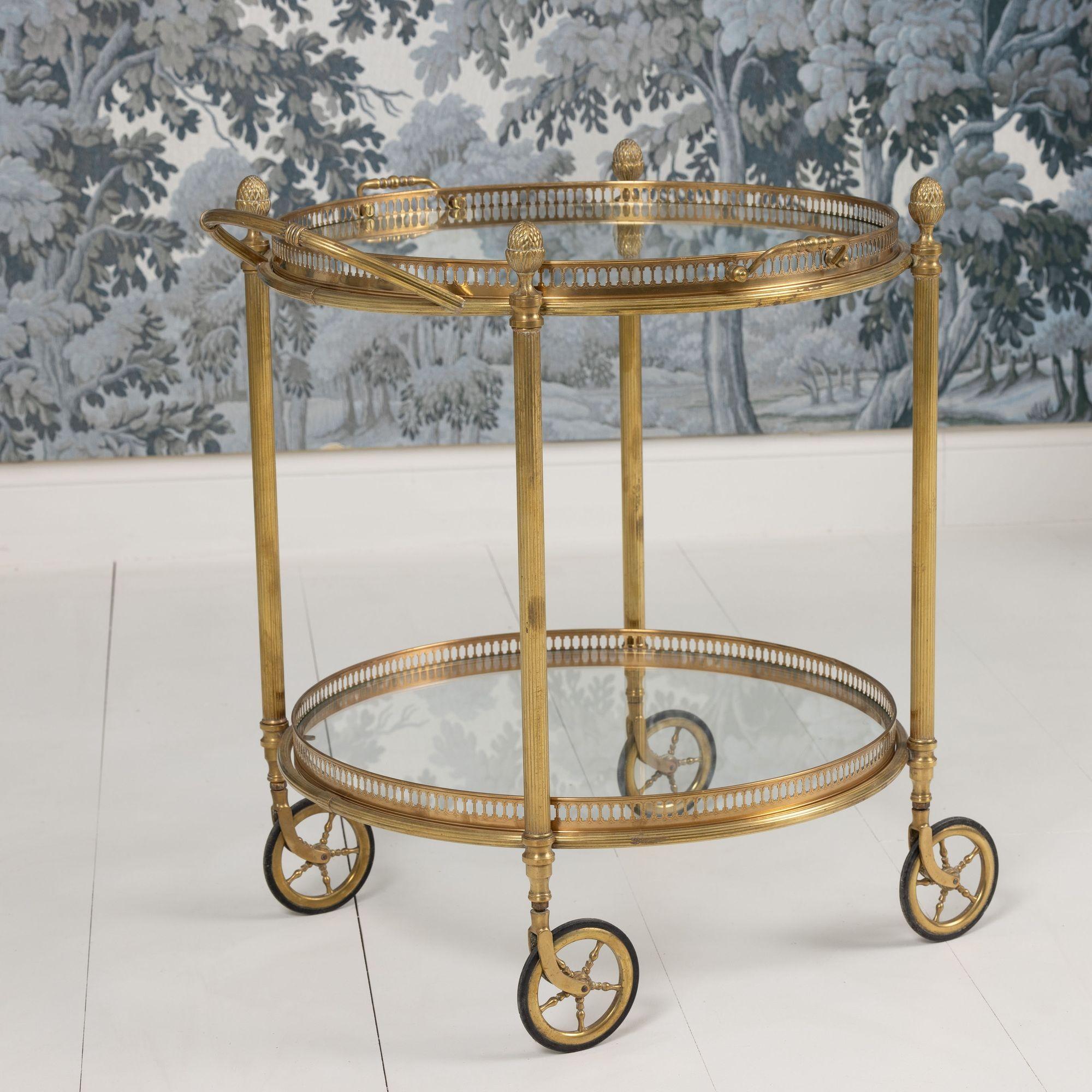 Carrello bar o carrello di servizio rotondo in stile neoclassico del designer francese Maison Baguès in ottone. Circa 1940. Vassoi in vetro originali superiori e inferiori rimovibili con galleria traforata. Il vassoio superiore ha due maniglie.