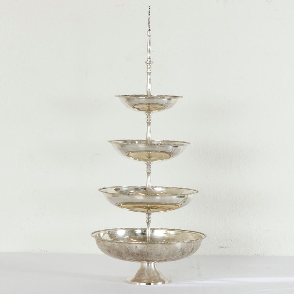 Standing at 36 inches in height, this French silver plate epergne or serving piece features four tiers joined by a central pillar. Beading adorns the rim of each concentric tier and a circular handle with a leaf motif at the top of the pillar allows