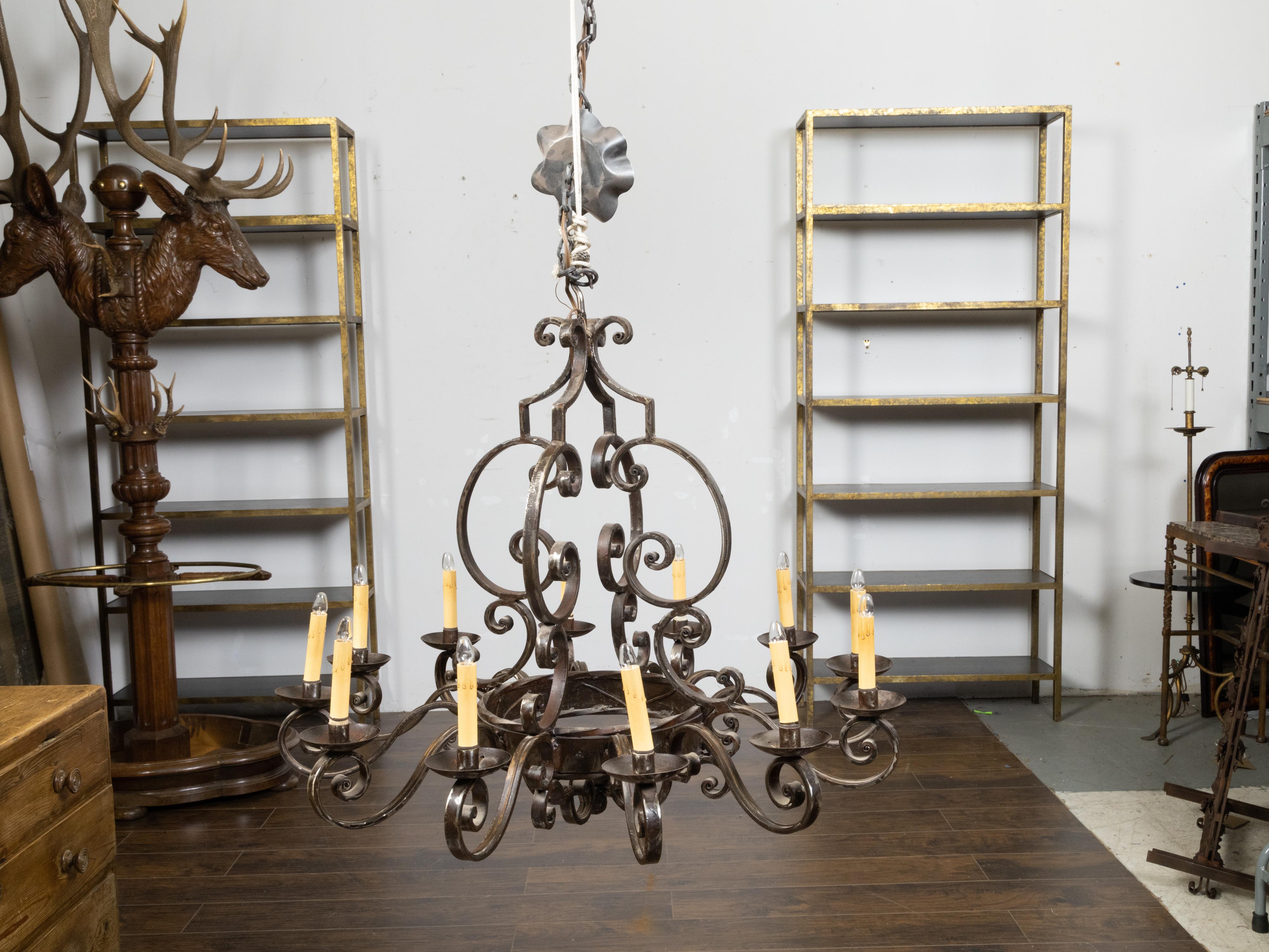 Lampadario vintage francese in acciaio della metà del XX secolo, con 12 luci, volute a C e a S e patina scura. Creato in Francia durante il periodo del Midcentury, questo lampadario in acciaio cattura la nostra attenzione con le sue belle
