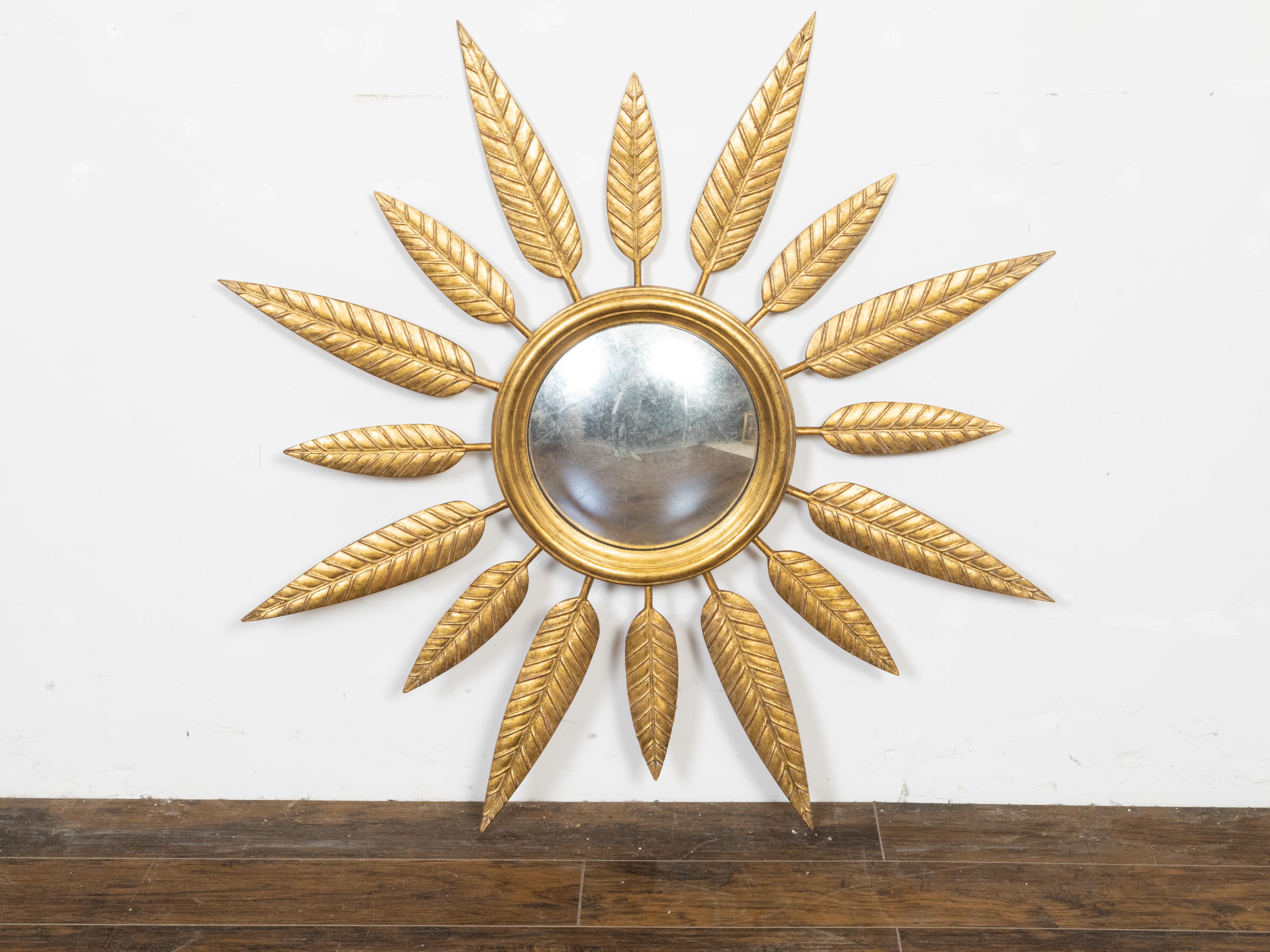 A vintage French gilt metal sunburst mirror from the mid 20th century, with convex plate, foliage leaves and molded frame. Created in France during the Midcentury period, this sunburst wall mirror features a circular frame with molded design,