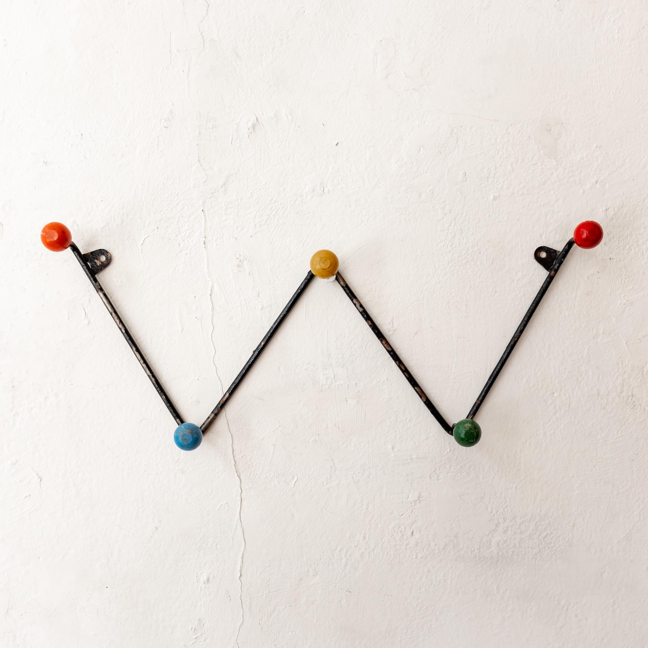 Wall mounted hat or coat rack from France. Solid rod iron frame with wood balls. Original paint with lovely patina. Two small brackets for screws allow for wall hanging. 1950s.