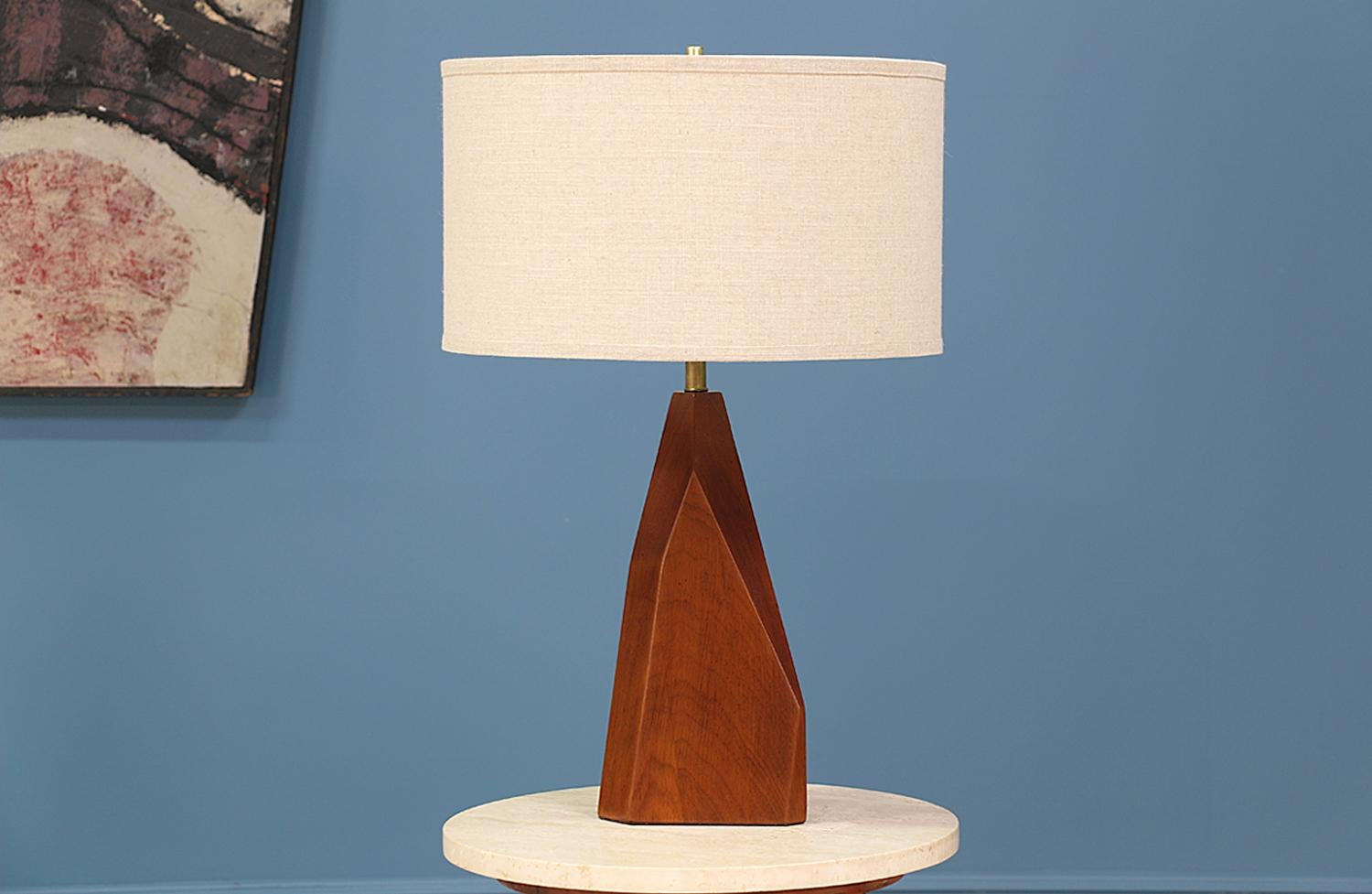 Mid-Century Modern table lamp designed and manufactured in the United States in the 1950’s. Featuring a geometric walnut foundation and new brass hardware, this items body combines different lines and cuts giving it an abstract shape. Newly rewired