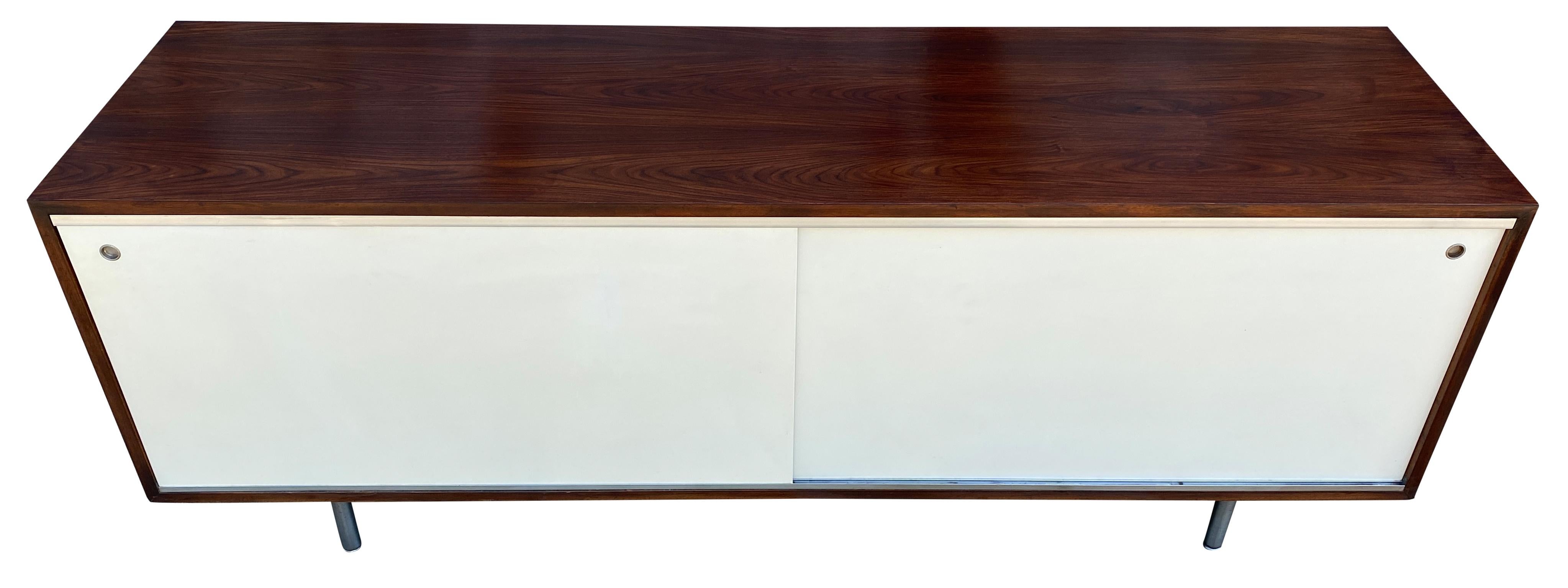 Wonderful low cabinet by Herman Miller designed by George Nelson #5803. This beautiful dark walnut low credenza features 2x front original white sliding doors with 4 sections inside and (2) adjustable shelves total with (1) slide out shelf on tracks