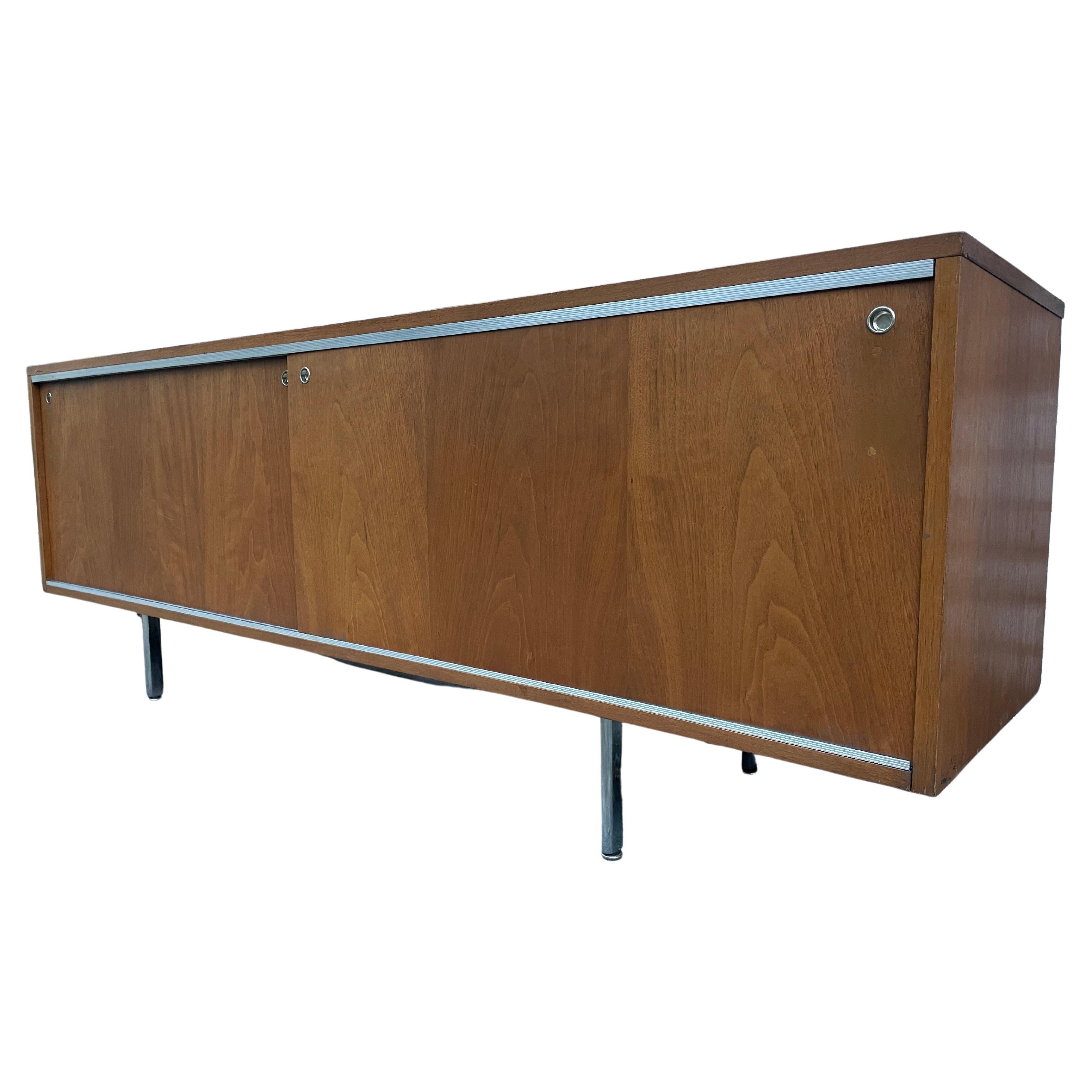 Wonderful low cabinet by Herman Miller designed by George Nelson. This beautiful brown walnut long low credenza features 2x front original walnut sliding doors with 2 sections inside and (1) adjustable shelf in each side. Sits on original chrome