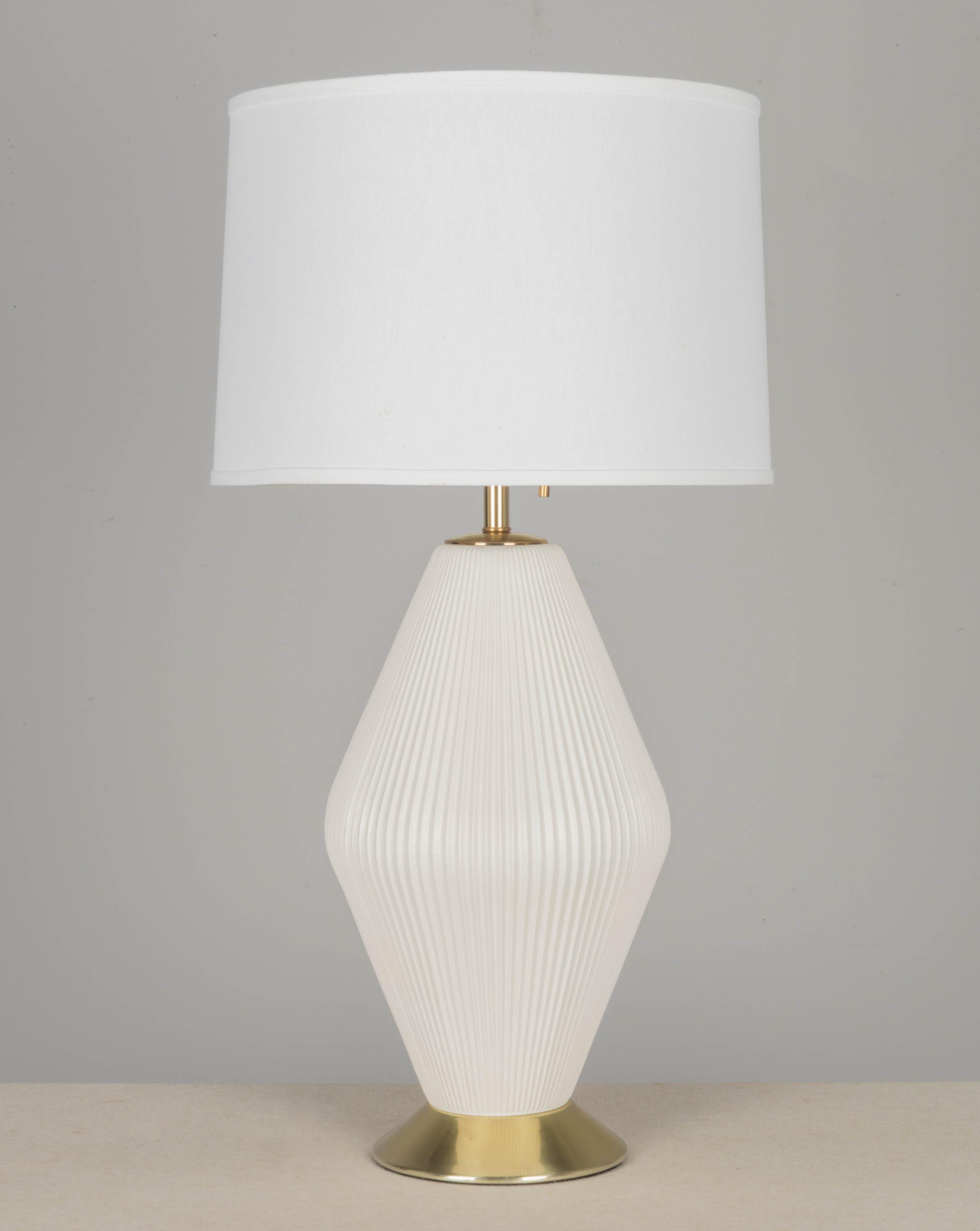 An iconic Midcentury Modern ceramic lamp by Gerald Thurston for Lightolier. Pleated ceramic body with matte white glaze. Brass plated base has light scratches with very small dent. Original 3-bulb socket with brass pull chain. New cord and brass