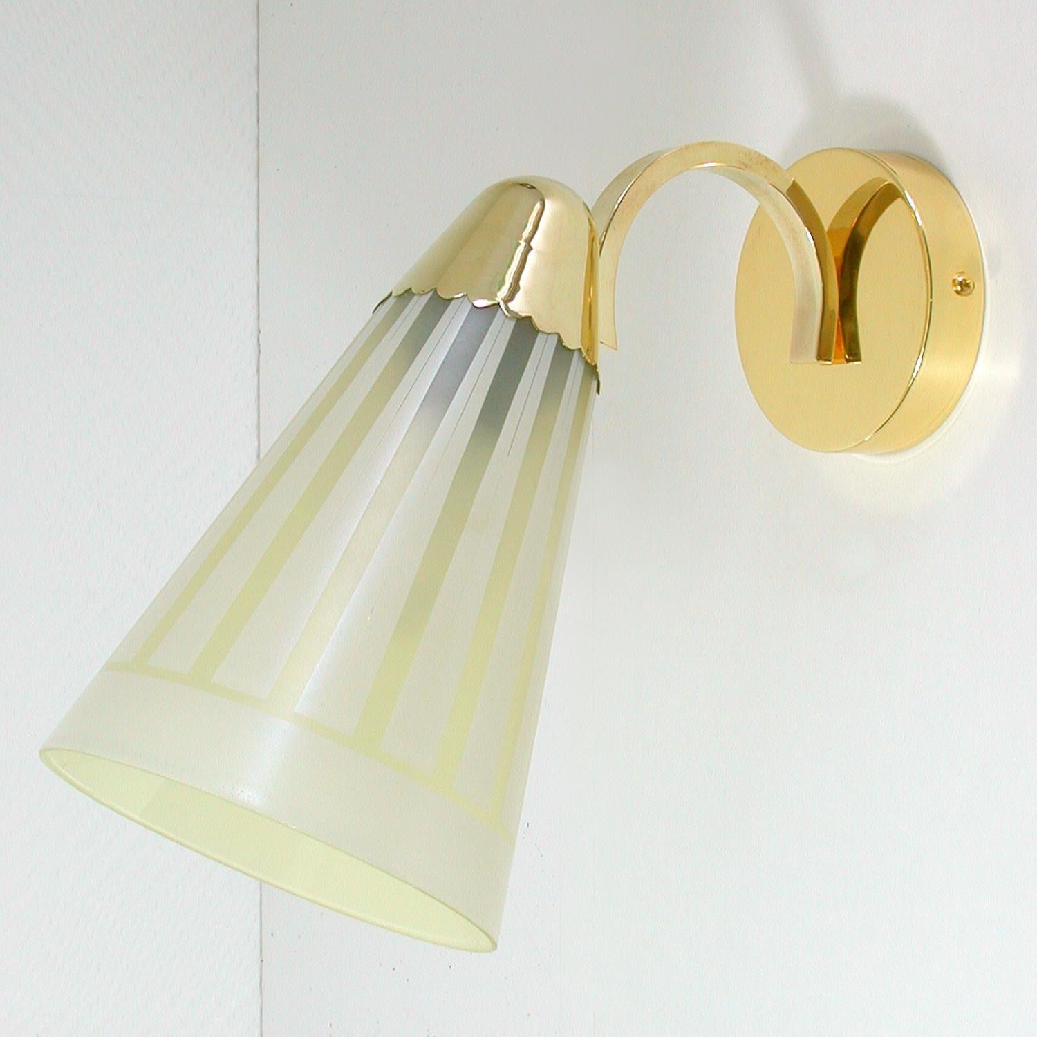 This elegant large midcentury wall light was designed and manufactured in Germany in the 1960s.

It is made of brass and has got a glass lamp shade. The lamp can be attached upright as well as shining downwards.

The lamp is in full working