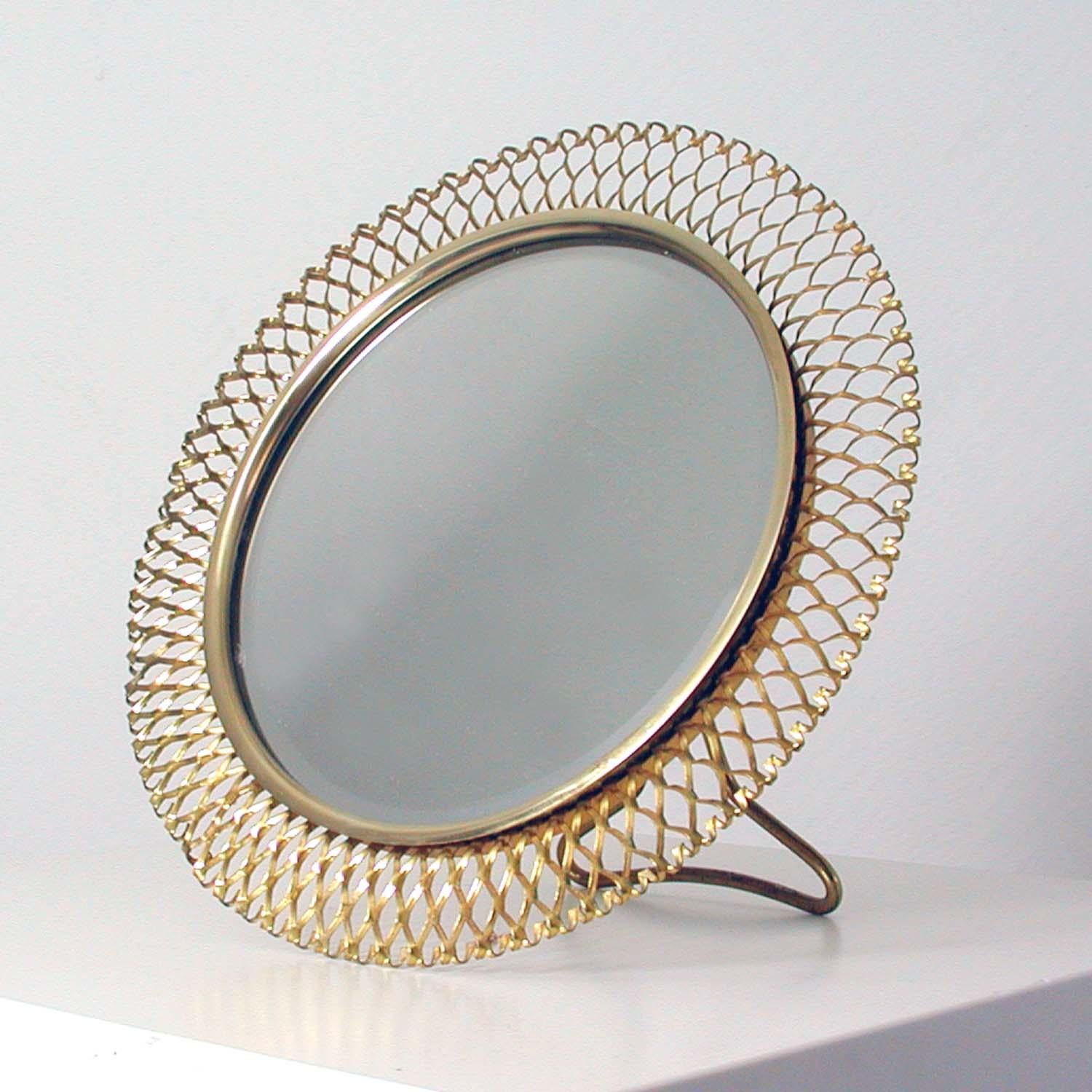This beautiful round midcentury table mirror was designed and manufactured in Germany in the 1950s by Vereinigte Werkstätten München. It is made of a brass stretched metal frame in the manner of French Designer Mathieu Matégot. The rear is made of