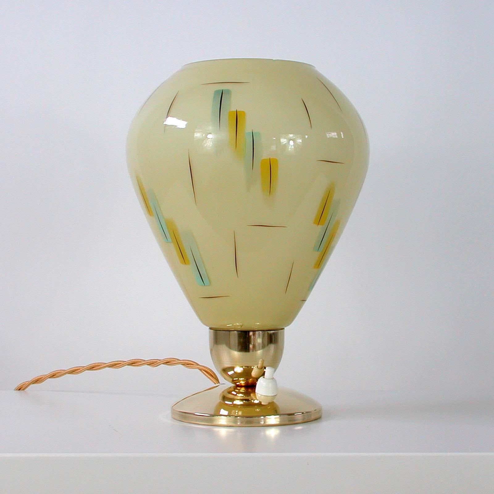 This vintage table lamp was designed and manufactured in Germany in the 1950s. It has got a brass foot and a cream colored and enameled opal glass lamp shade in typical 