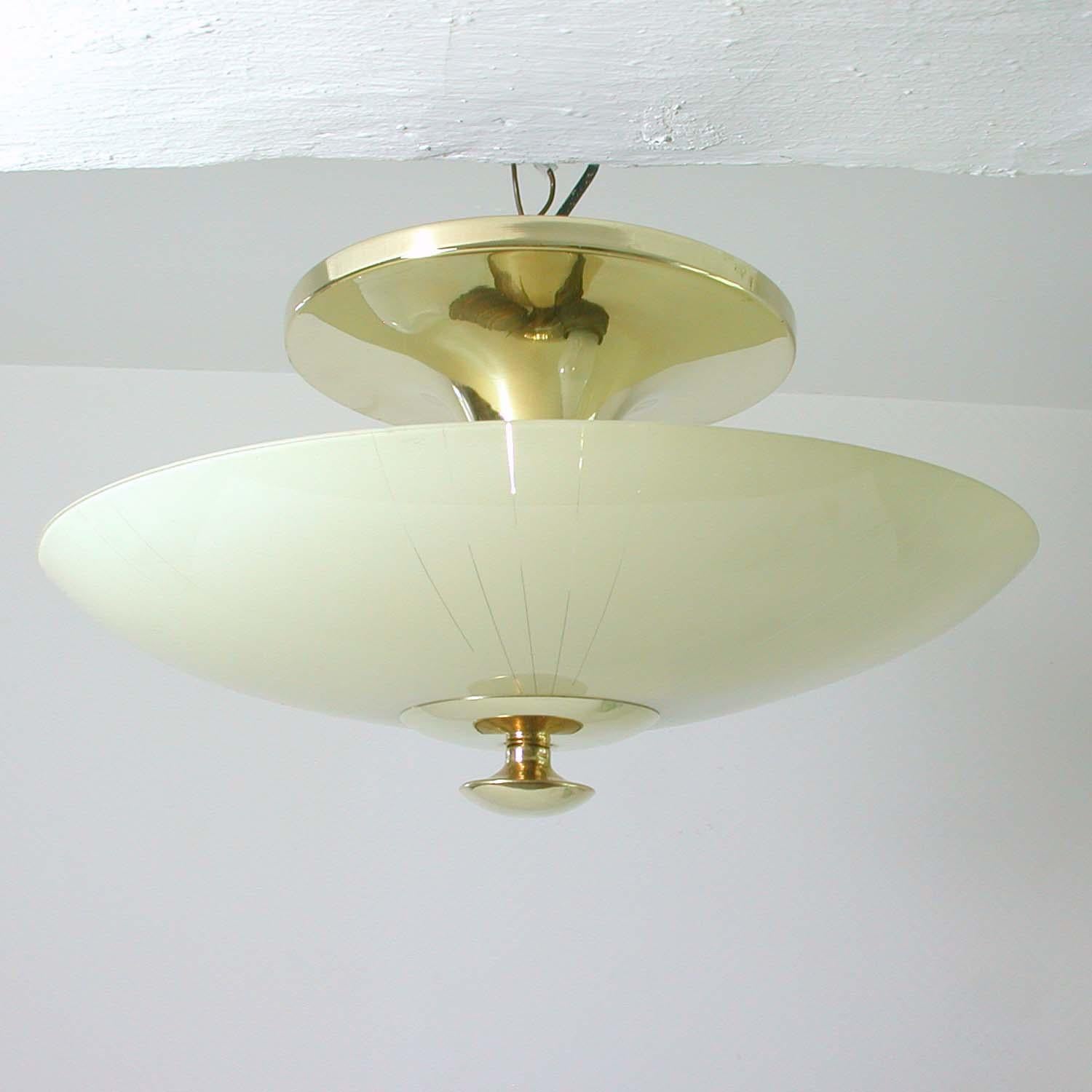 This Bauhaus inspired flush mount was designed and manufactured in Germany in the 1950s.

The lampshade is made of cream colored opaline glass. The base is polished brass. 

The lamp has got 2 brass sockets and works with standard E27 Edison