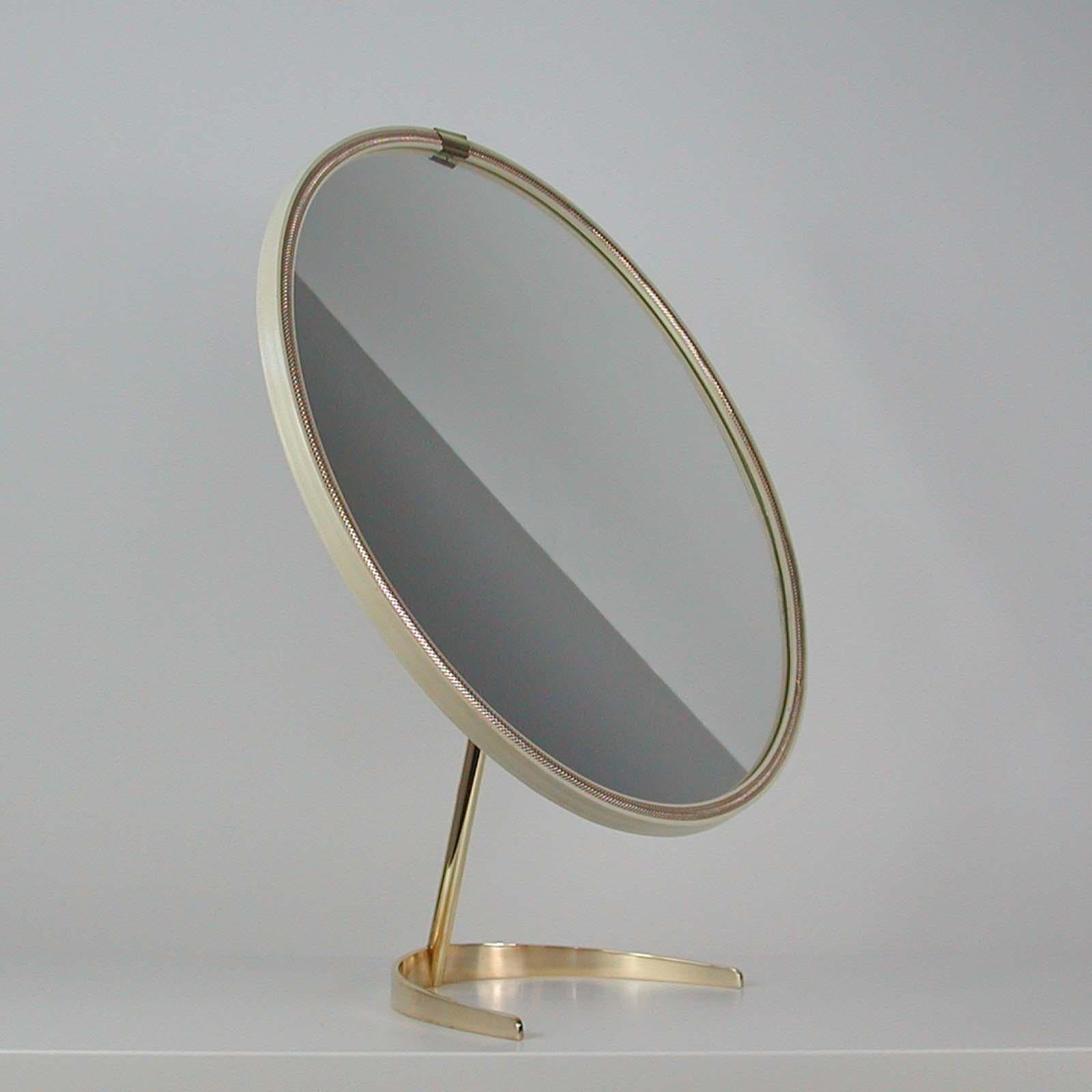 This awesome large vanity or table mirror was designed and manufactured in Germany in the 1950s by Vereinigte Werkstätten Munich. It features an off-white colored plastic frame with perforated brass decoration on a semicircular brass foot. The