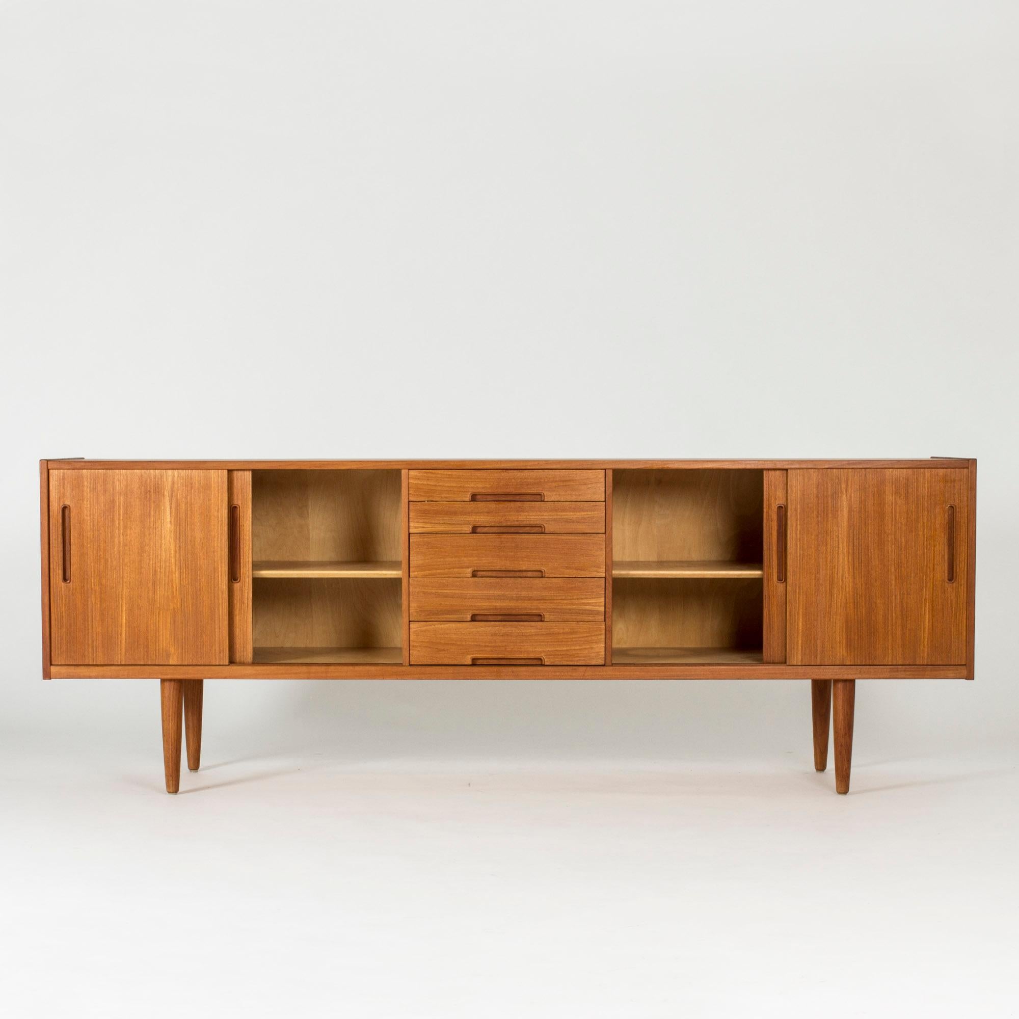 “Gigant” sideboard by Nils Jonsson. Made from teak, with a central chest of drawers and shelves on each side with sliding doors. Cool effect of the direction of the wood grain which is vertical on the doors and horizontal on the drawers.