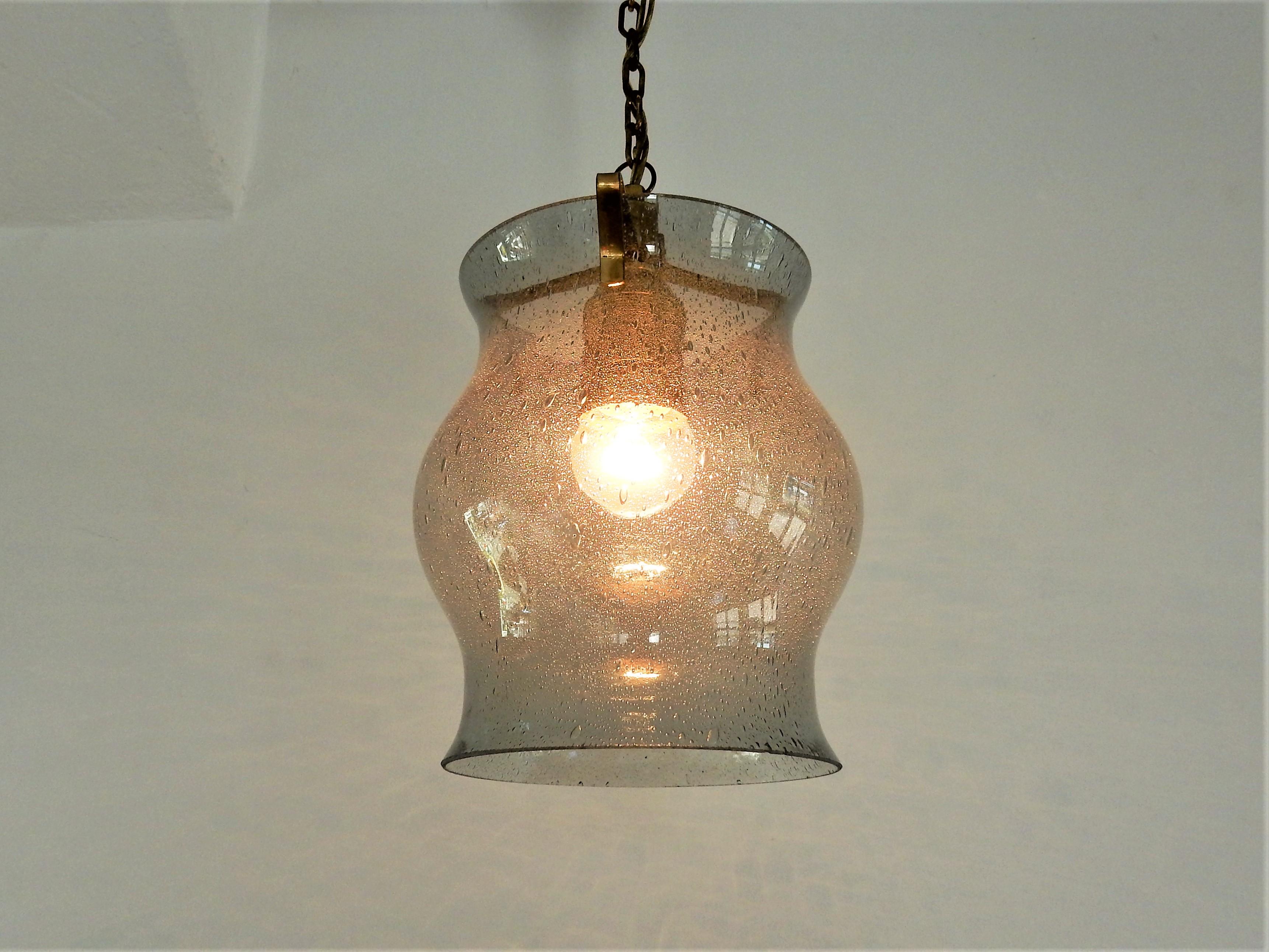 This is a very elegant early midcentury pendant lamp made of bubble glass on a brass suspension. It is in the style of Fagerlund and Orrefors. The lamp is in a good condition with minor signs of age and use. Looks great in a hall way or bedroom for