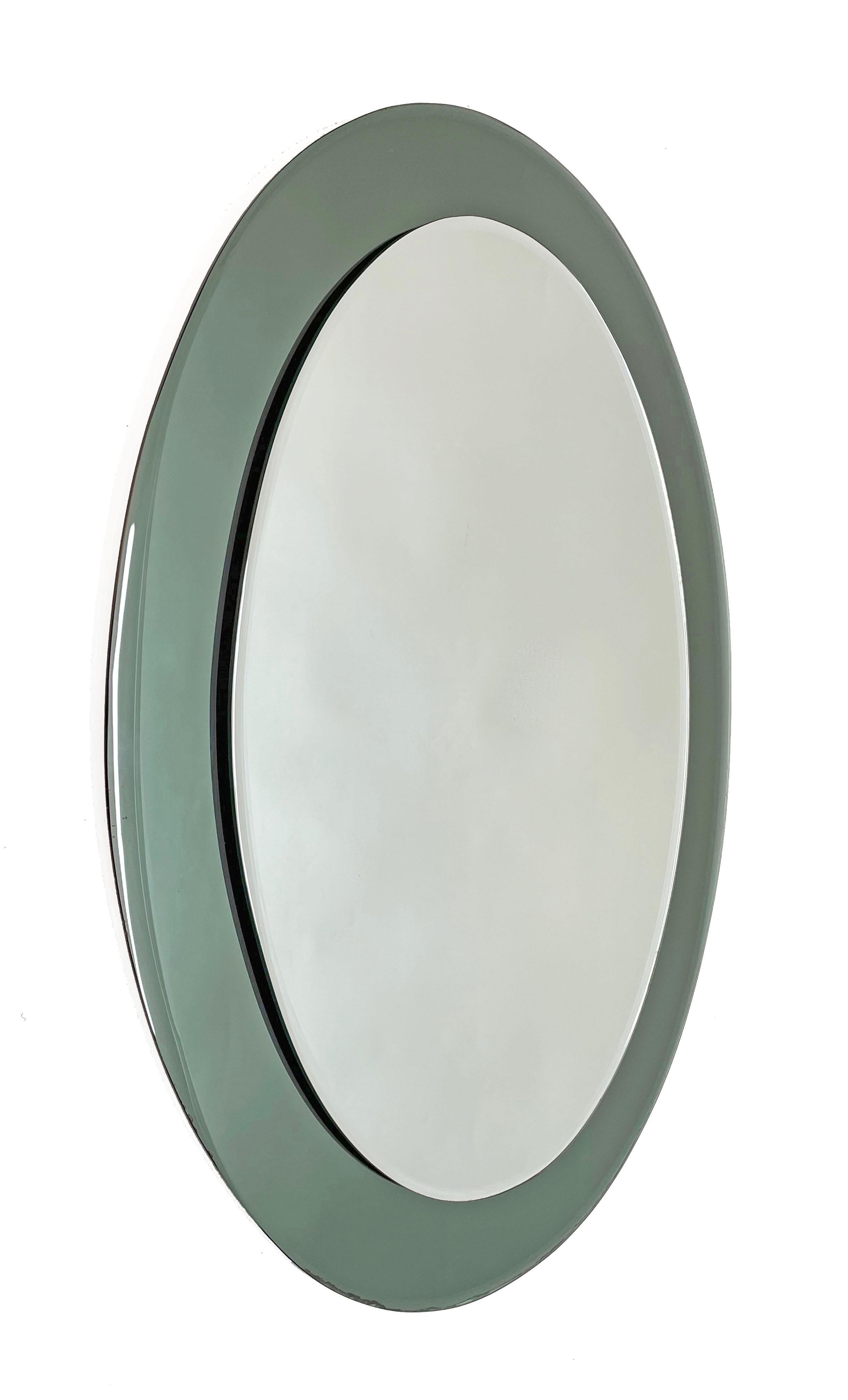 Wonderful midcentury oval wall glass framed mirror. This amazing item was produced in Italy during the 1960s and its design is attributed to Cristal Art.

In its essential, pure midcentury design and lines, it features a smoked green glass frame