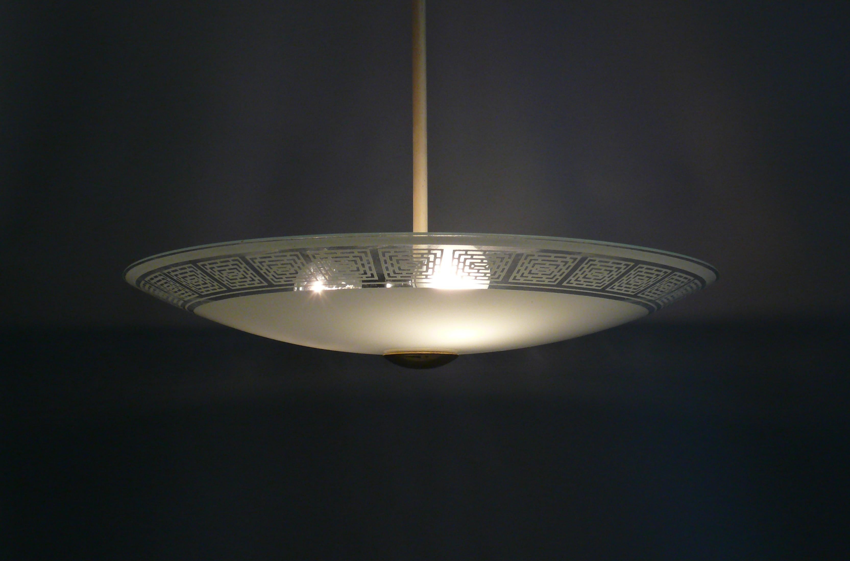 Very large rod pendant lamp from the 1950s with a bowl-shaped shade and coated rod. The UFO-shaped glass shade has a blue-gray color and geometric patterns with transparent areas around the edge. The lower end button is made of brass or
